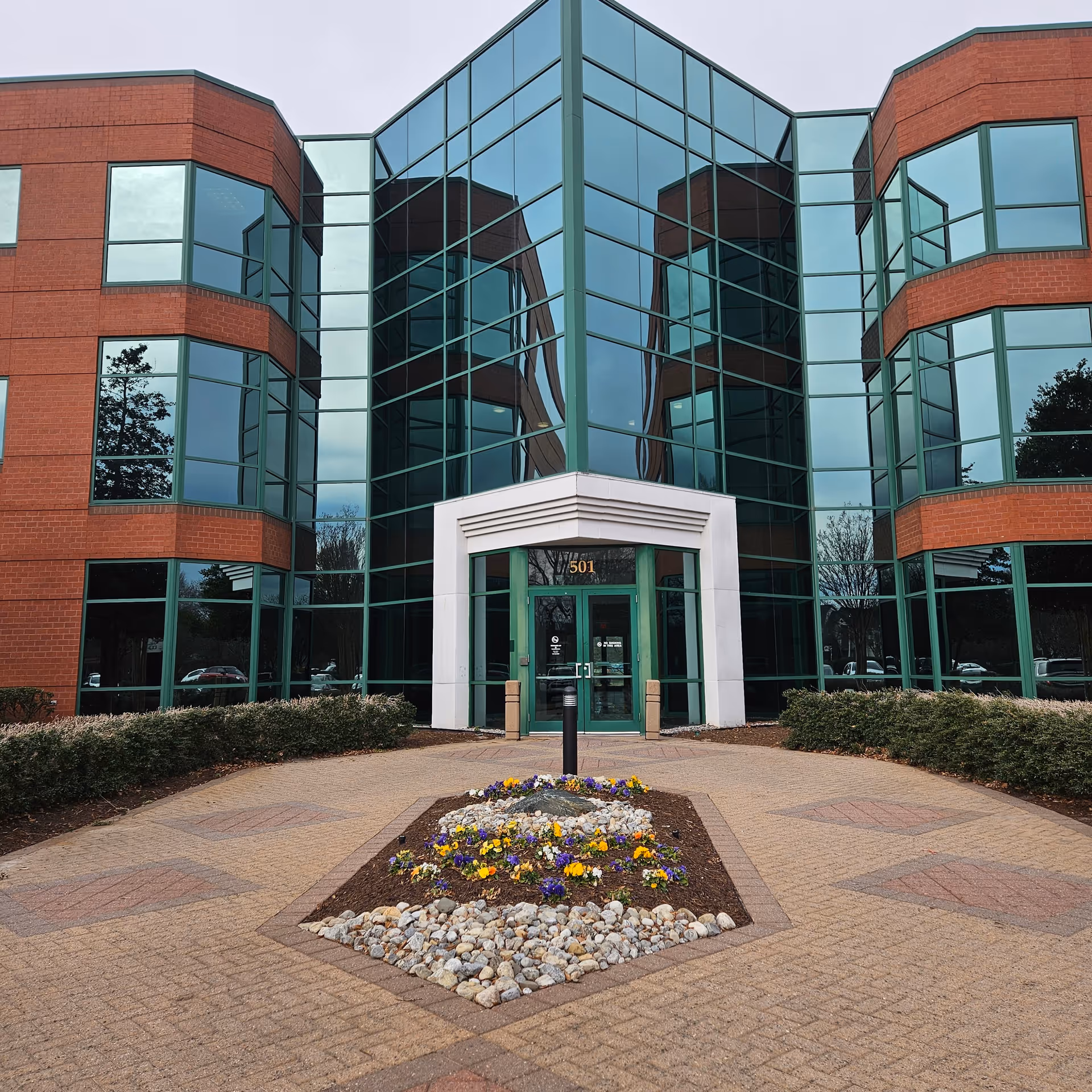 Front view of brick-and-glass senior living facility entrance with landscaped flower bed.