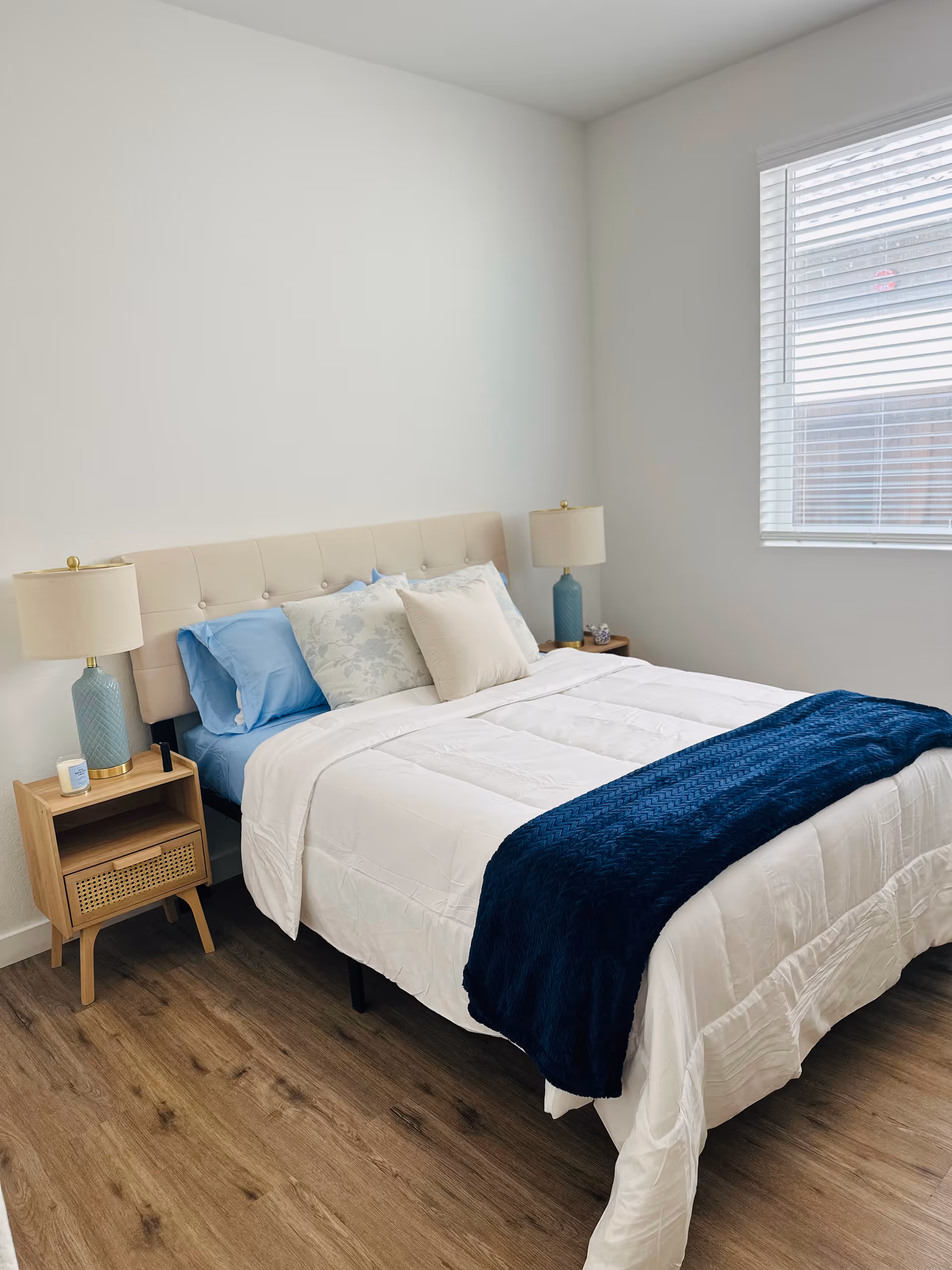 Cozy bedroom with a queen bed, two nightstands, lamps, and a window with blinds.