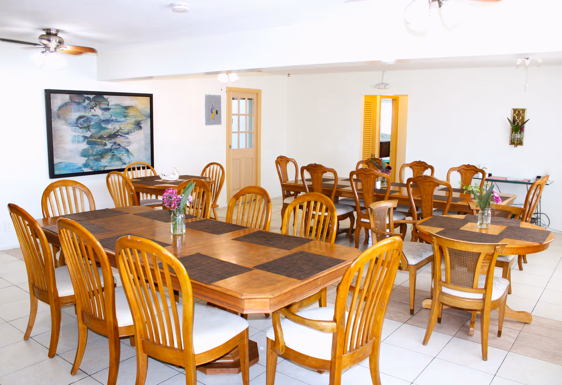 Bright dining hall at Tropical Garden Villas with wooden tables, chairs, and floral centerpieces.