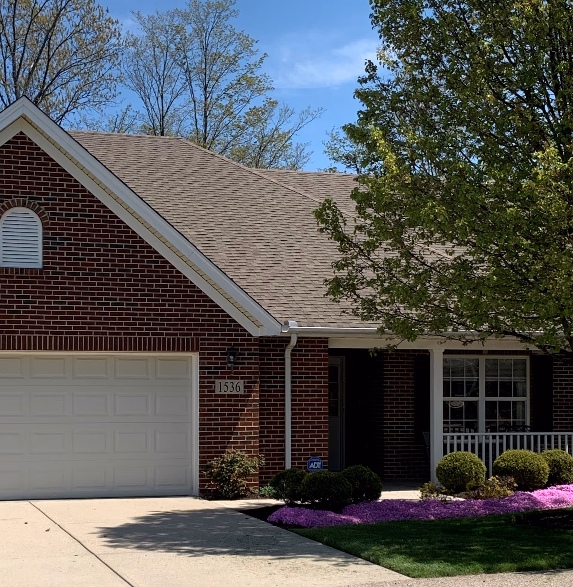 Brick residential front with garage, entryway, and landscaped lawn and purple flowers.