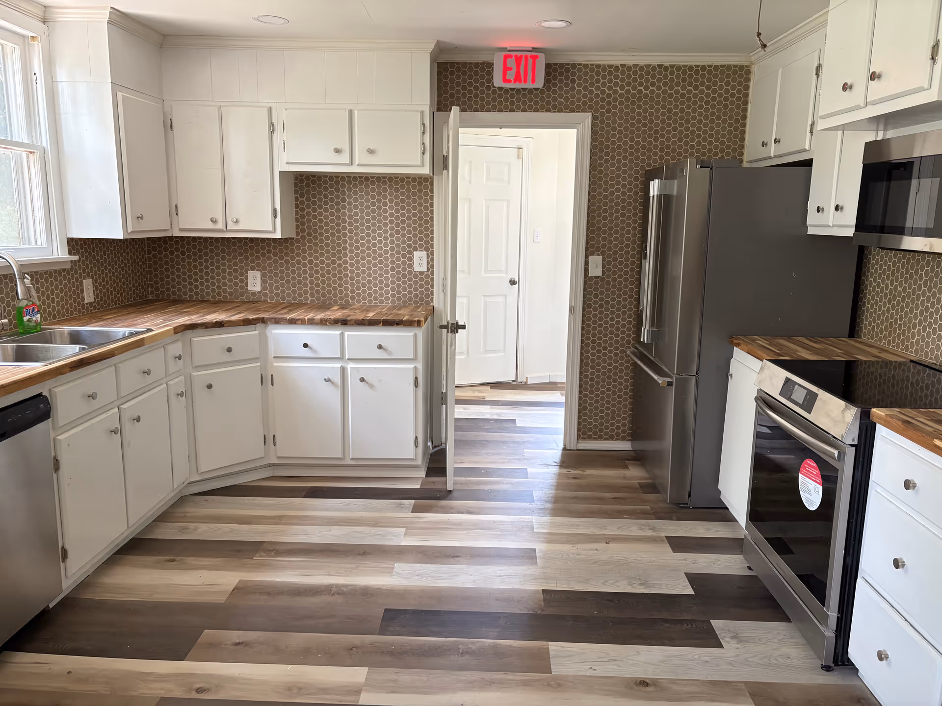 Bright kitchen with white cabinets, stainless appliances, wood countertops, and hex-patterned backsplash.