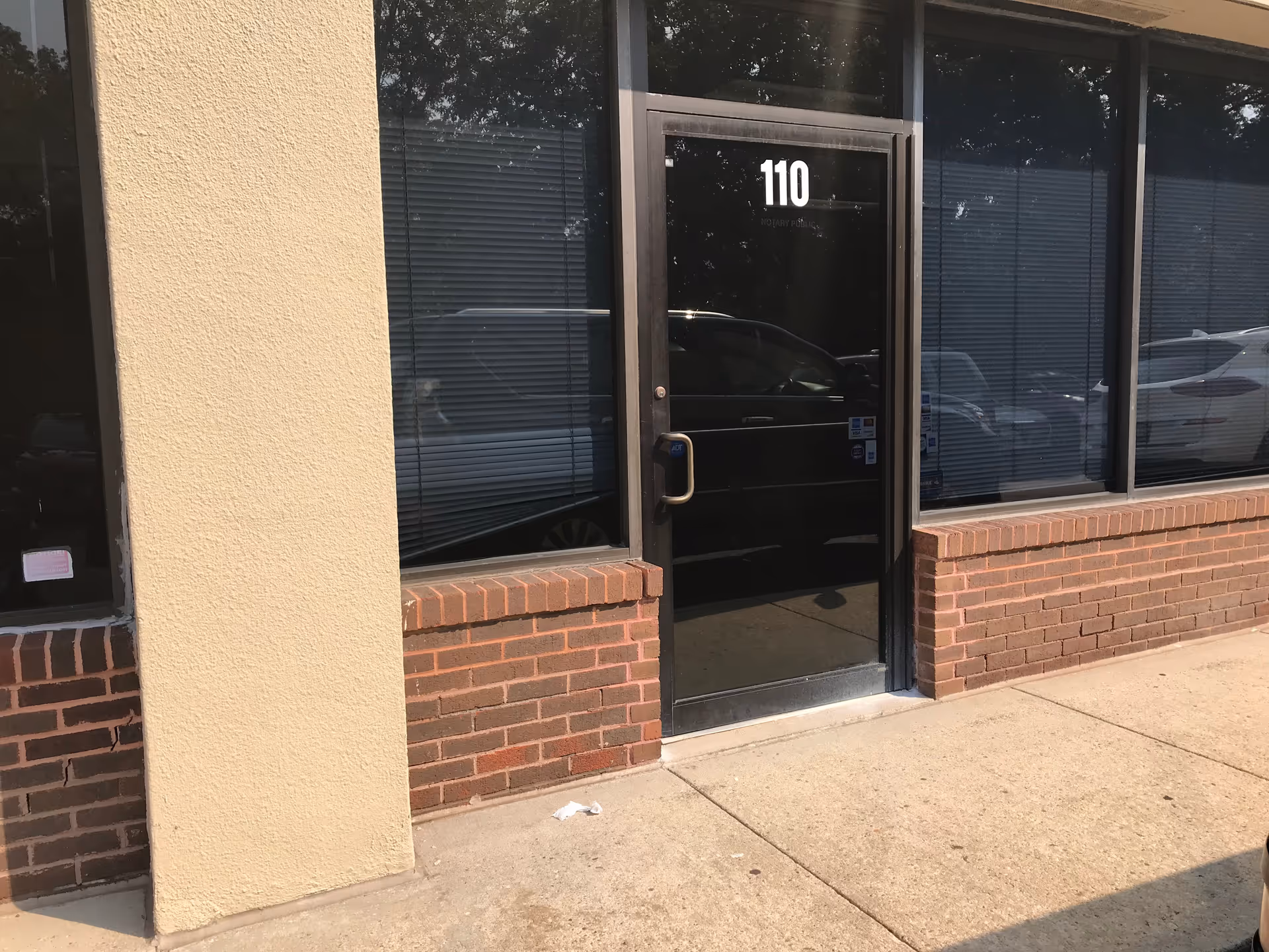 Exterior view of a facility entrance with a black door marked 110, brick and beige column.