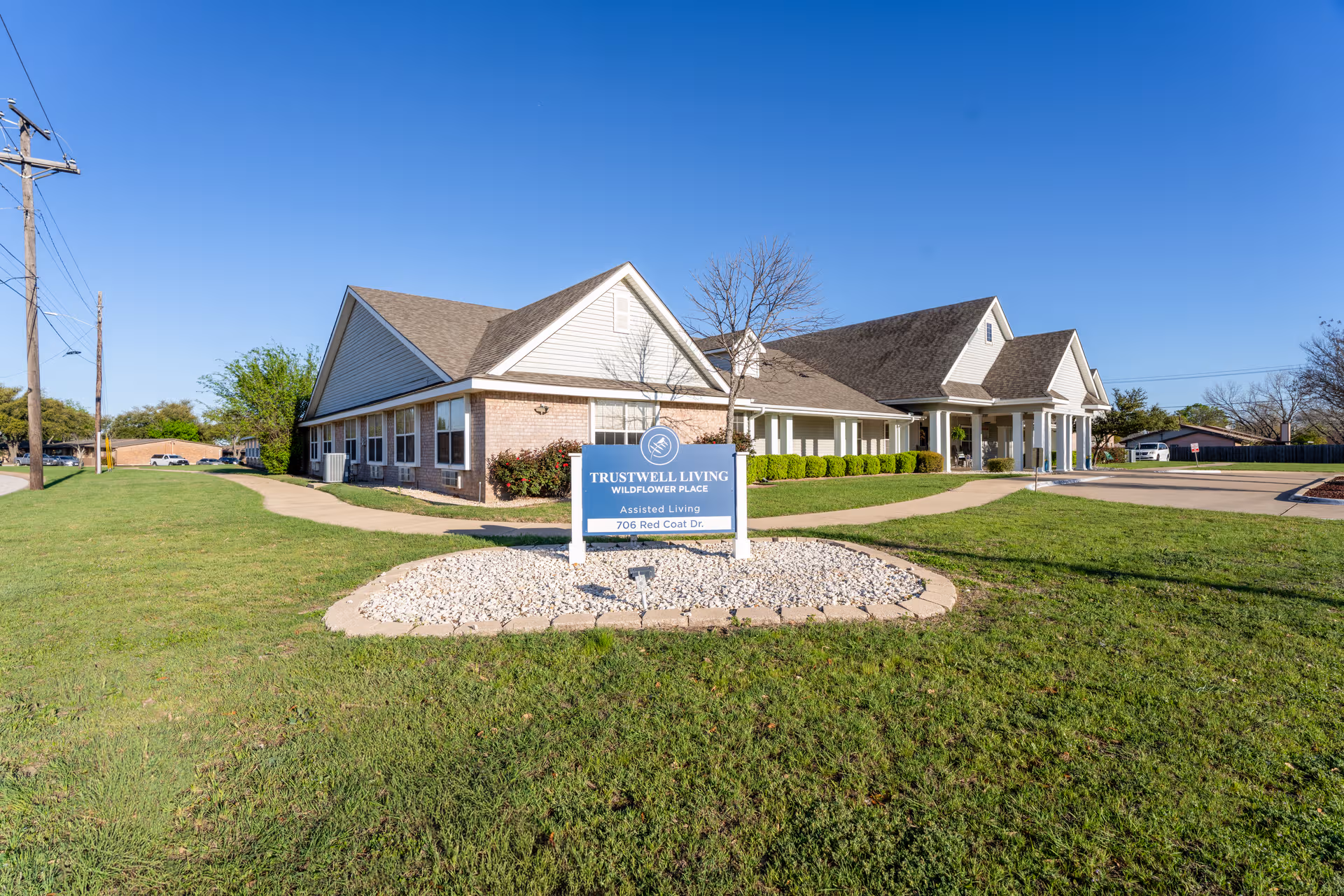 Exterior view of Trustwell Living at Wildflower Place with blue sky and sign.