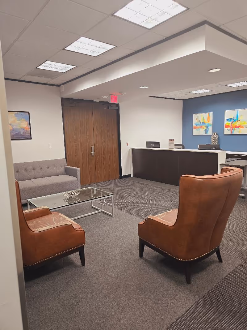 Lobby seating area with brown leather chairs and a reception desk.