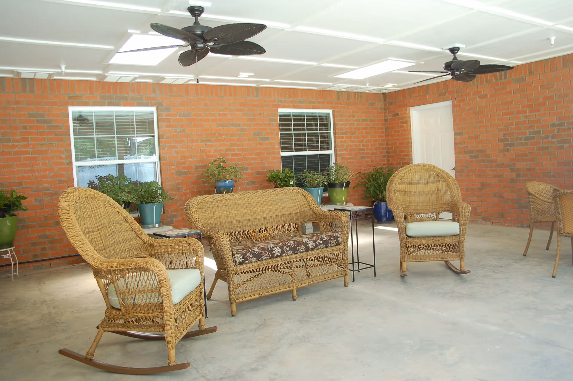 Covered outdoor patio with wicker seating, potted plants, and brick walls.