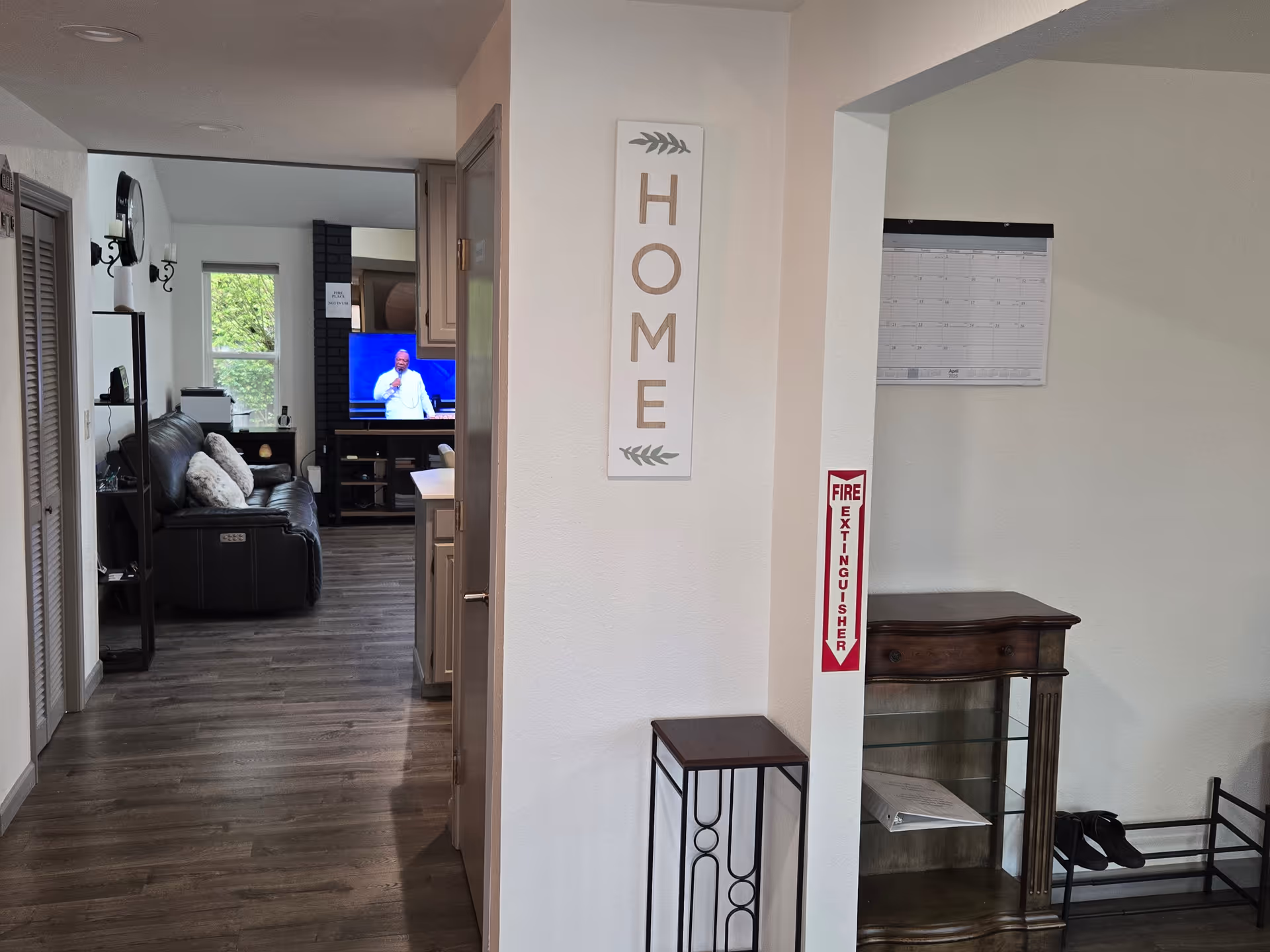 Interior hallway leading to a living room with a leather sofa, TV, and HOME sign.