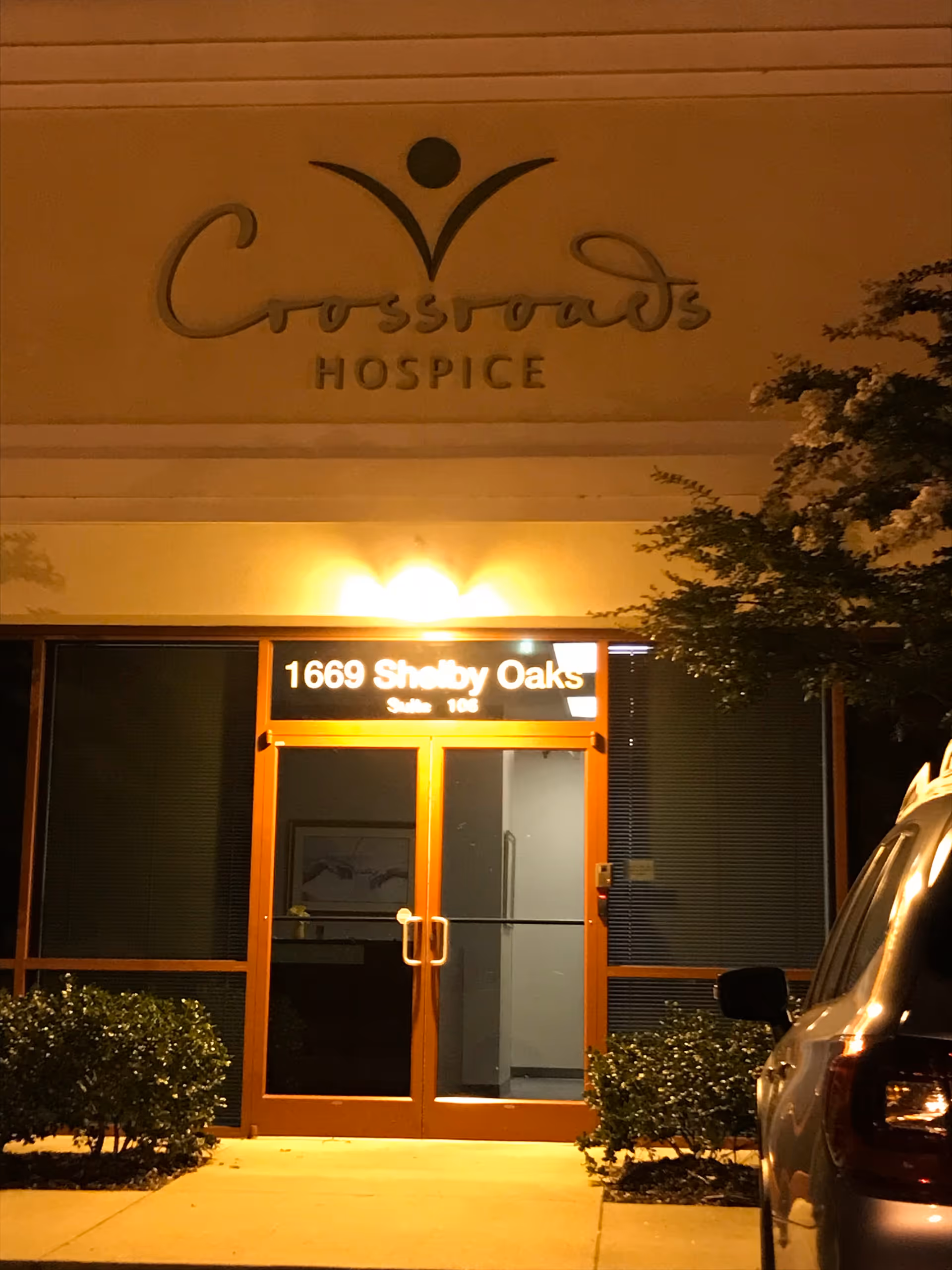 Night exterior of Crossroads Hospice building entrance with illuminated sign and glass doors.