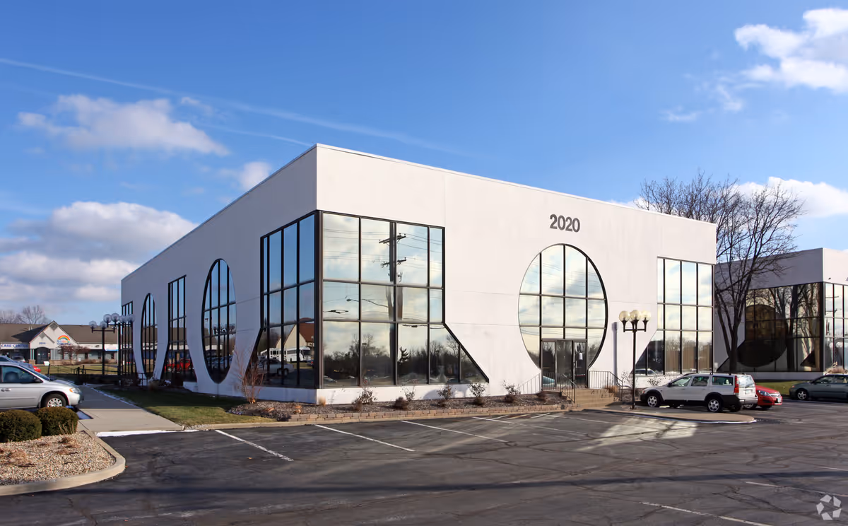 Modern white building with large circular windows and a parking lot in front.