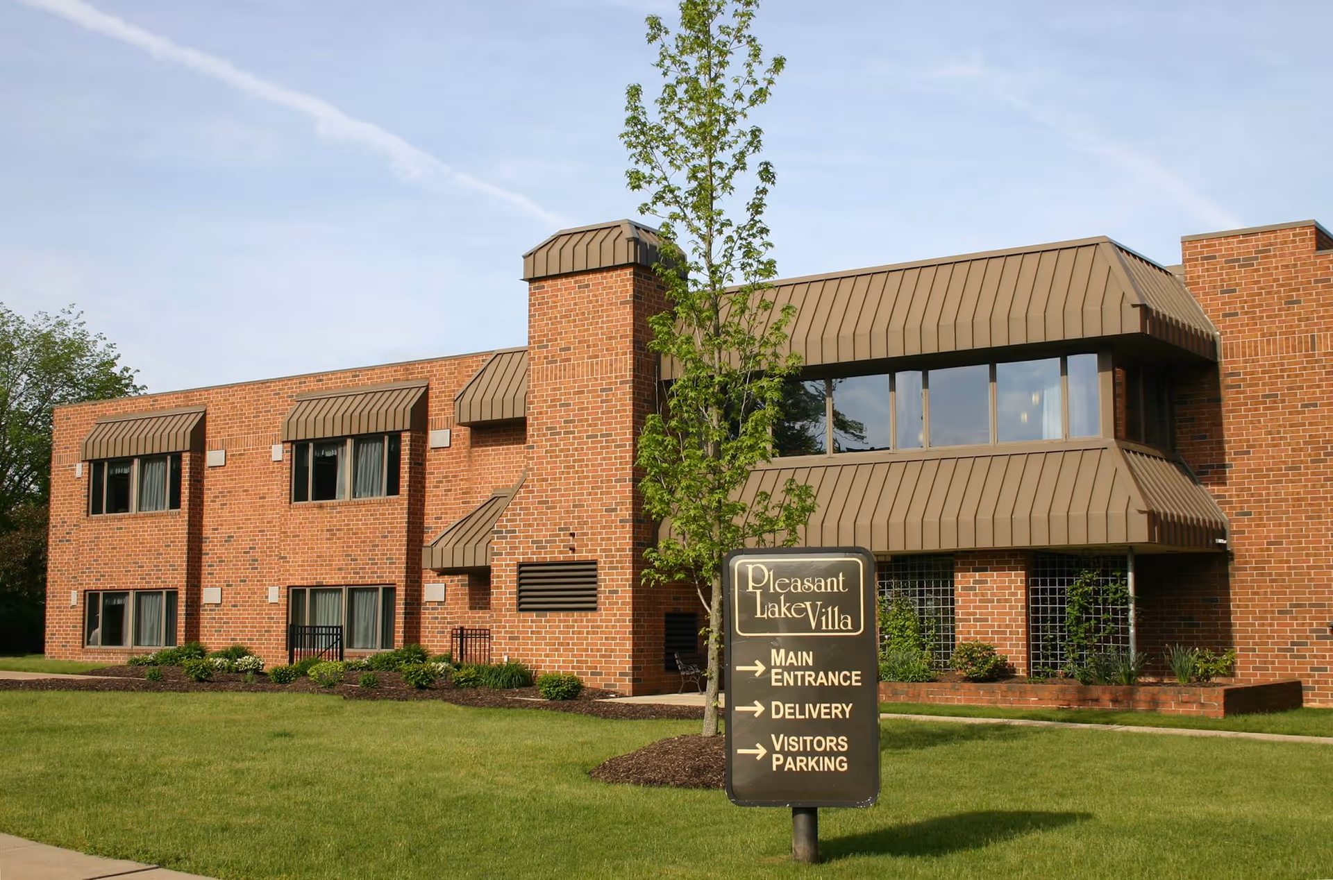 A brick senior living facility named Pleasant Lake Villa with a front sign and landscaped lawn.