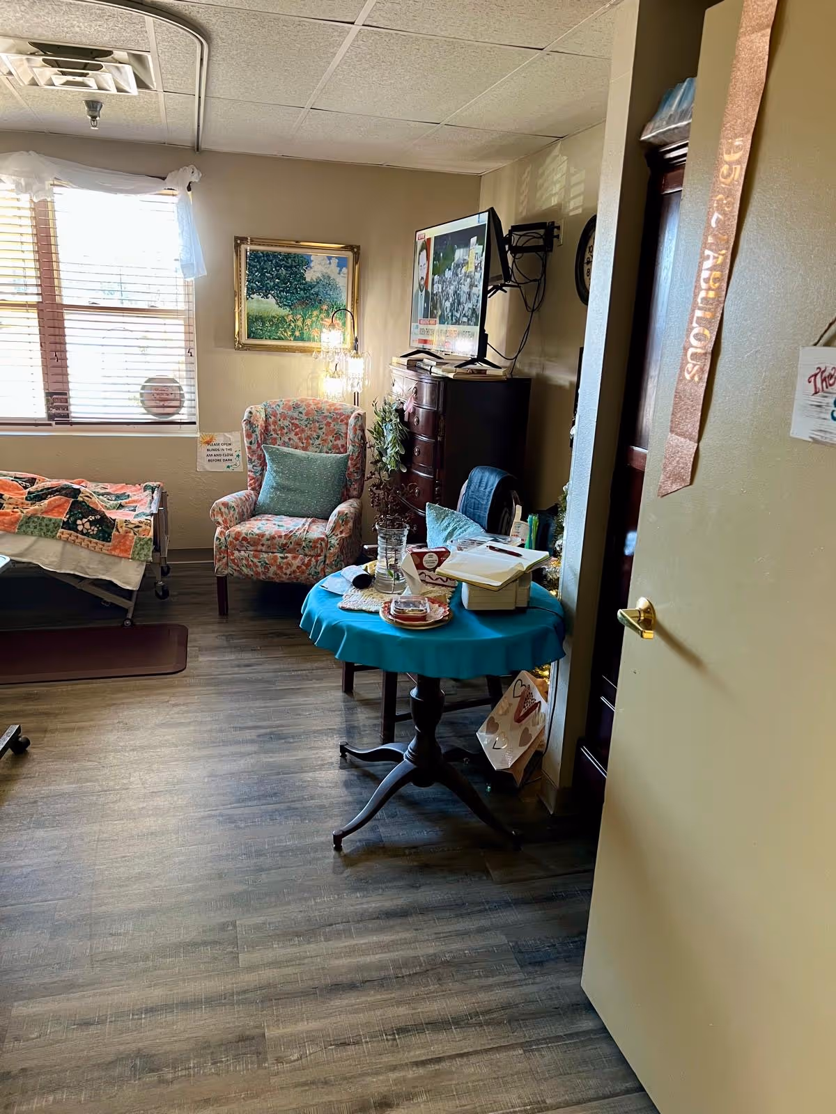 Cozy senior living interior with quilted bed, floral chair, TV, and teal round table.
