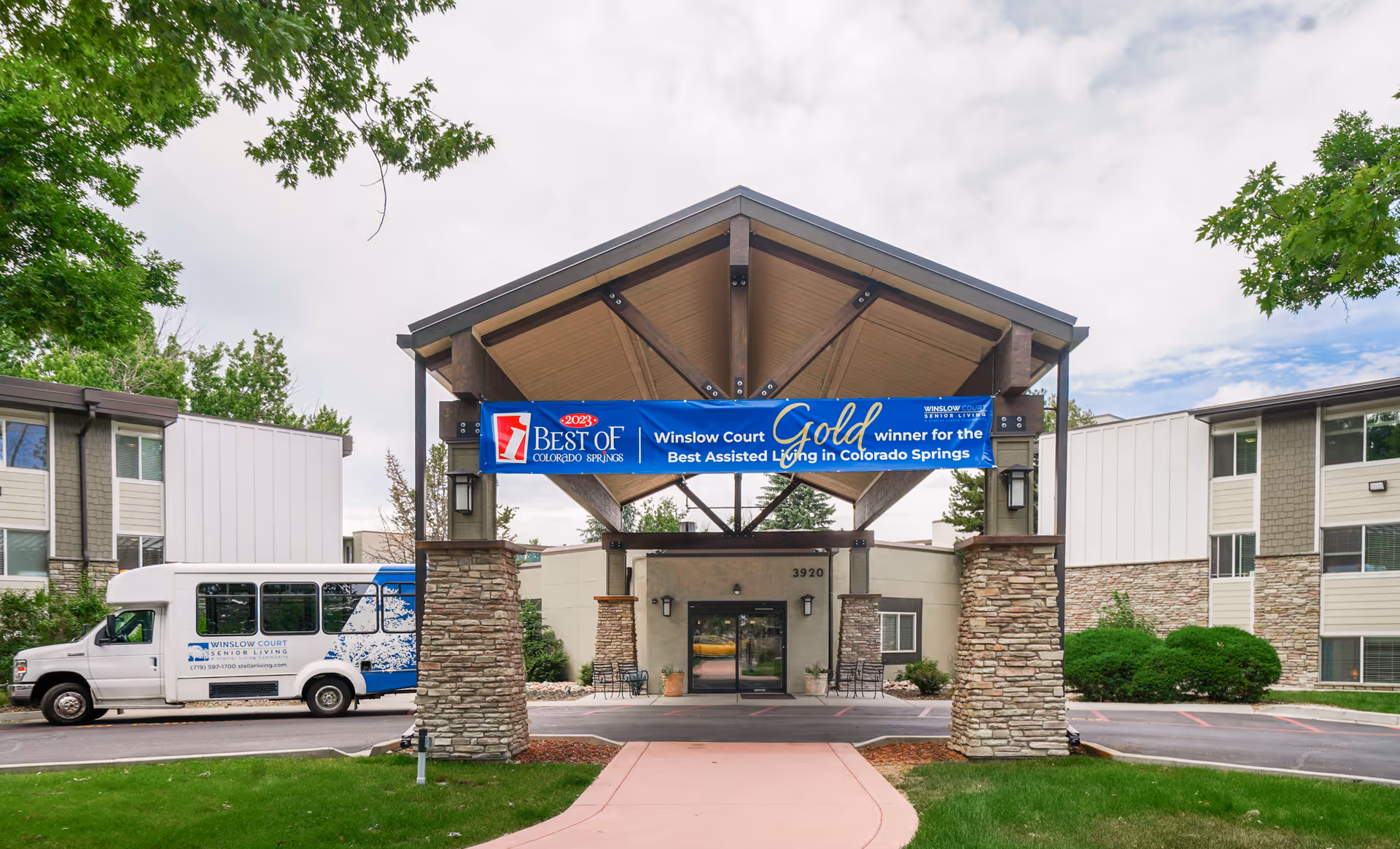 Front entrance of Winslow Court Assisted & Senior Living with a covered porte-cochere, award banner and a shuttle van parked to the left.