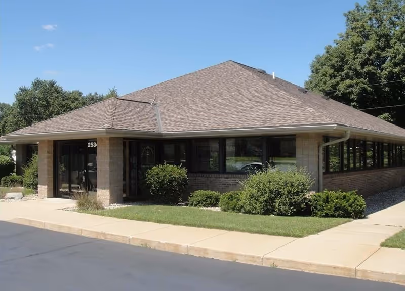 Single-story brick building with large windows and a manicured entrance lawn.
