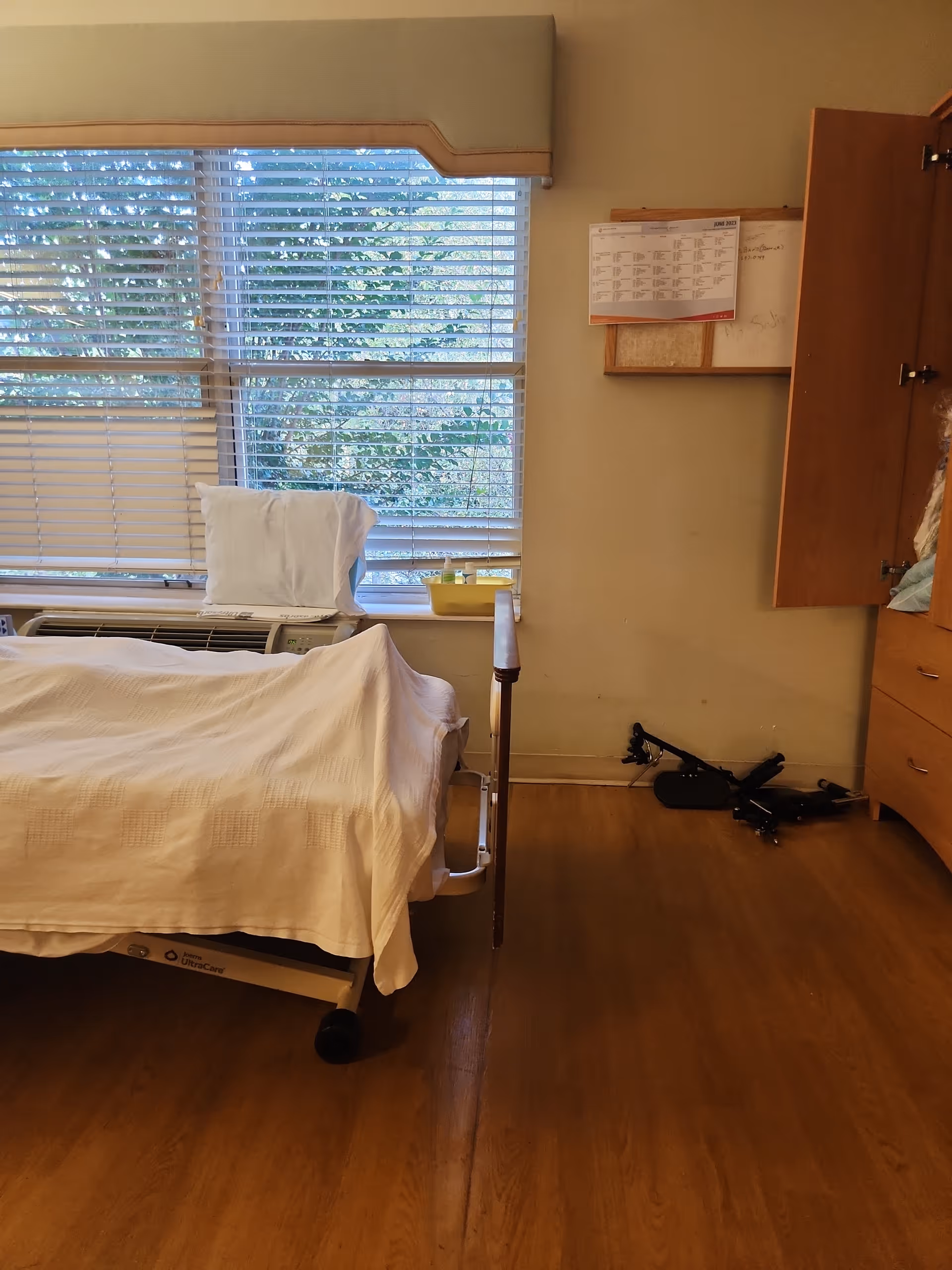 A hospital-style bed with white linens in a bright patient bedroom.