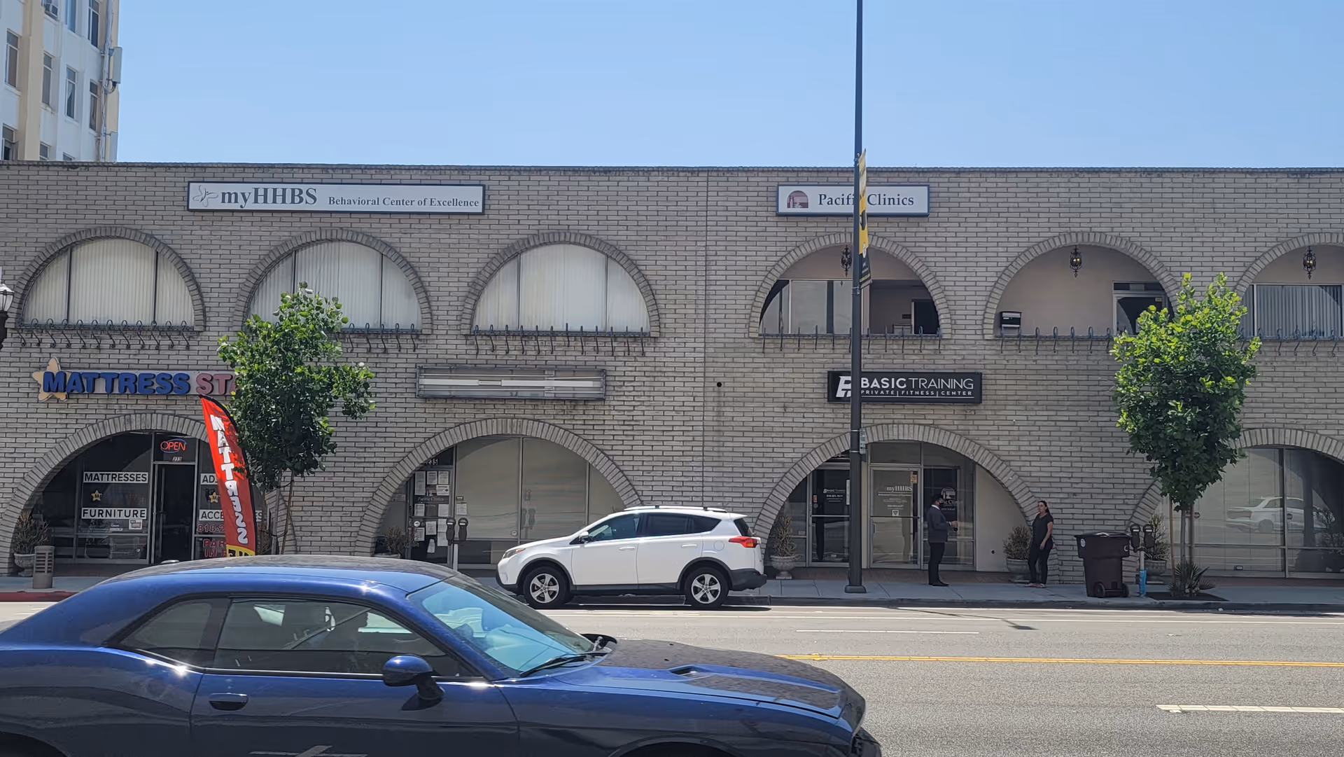 A brick storefront building along a street with myHHBS signage and parked cars.