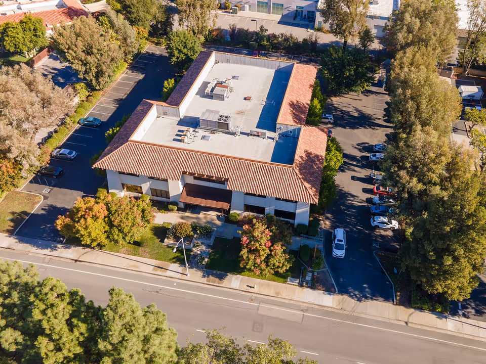 Aerial view of a U-shaped building with red-tiled roof, parking lots, and trees.