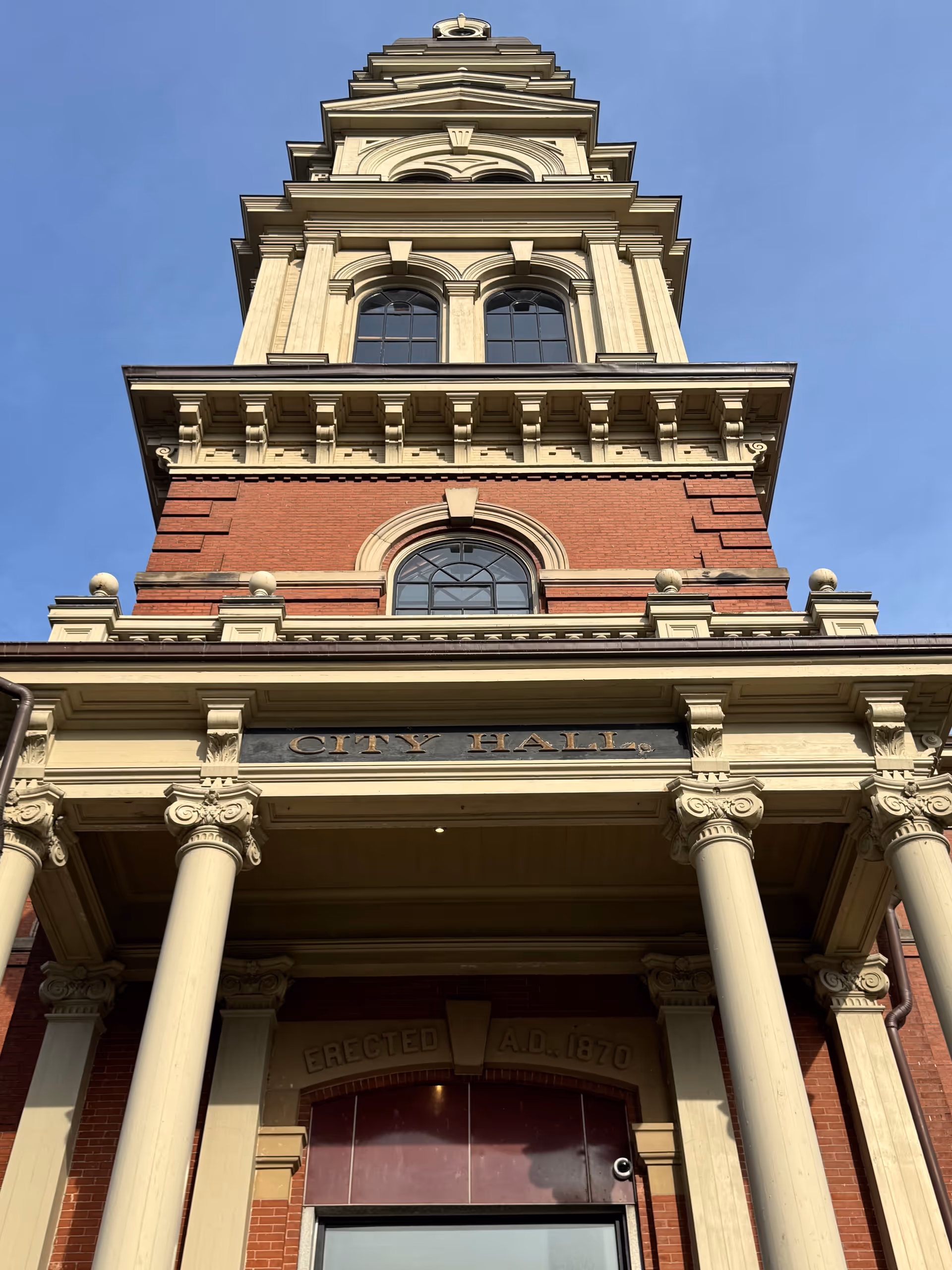 Tall historic city hall building with columns, arches, and a clock tower against blue sky.