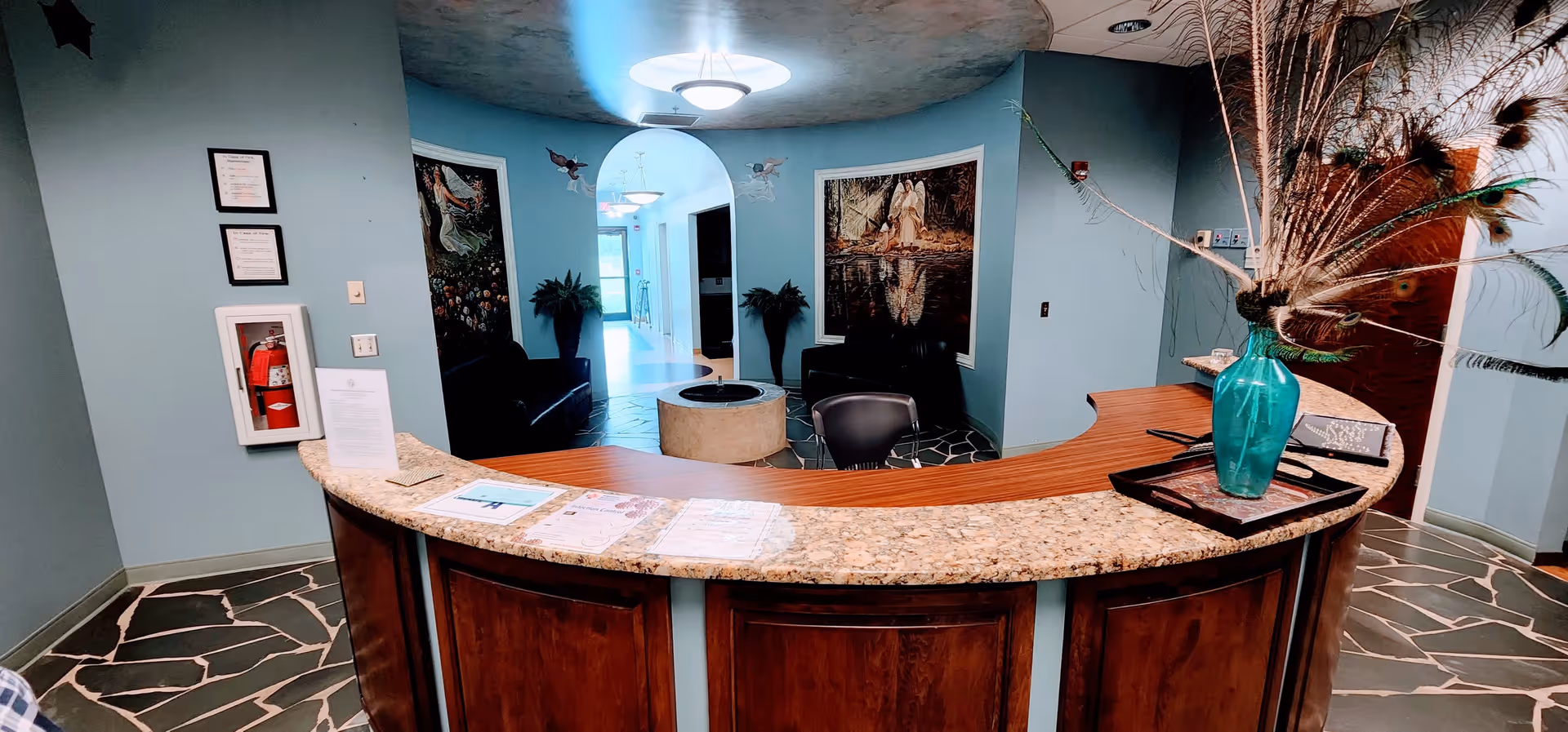 Curved granite reception desk in a turquoise lobby with seating and decorative vase.