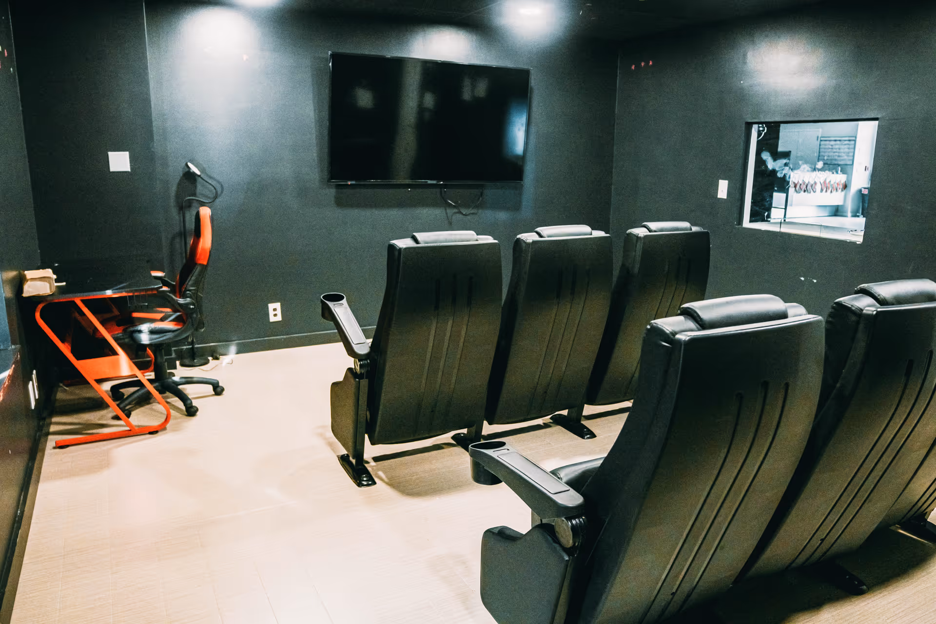 A dark screening room with black theater seats and a wall-mounted TV.