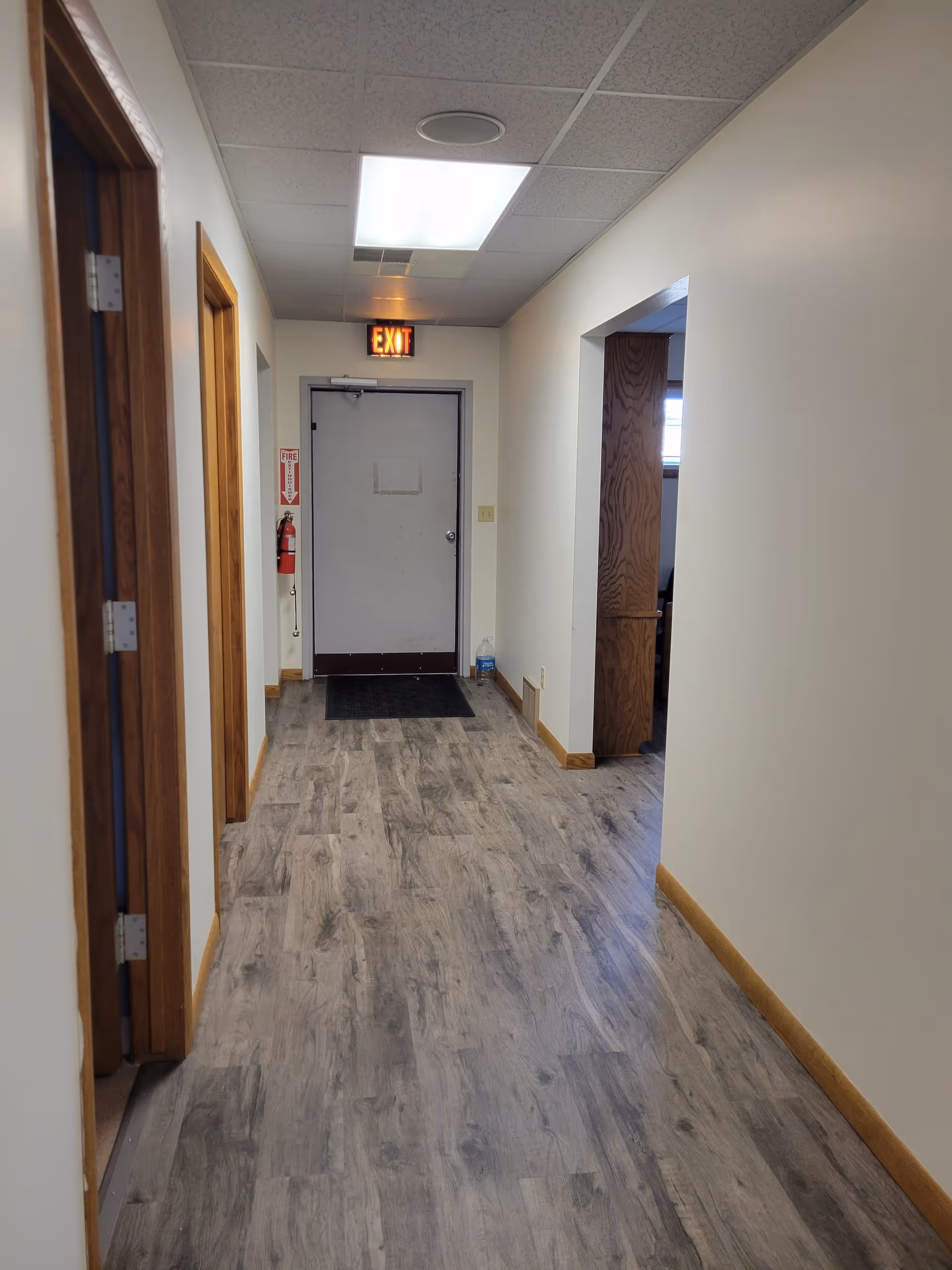 Interior hallway with doors on both sides, exit sign, and ceiling lights.