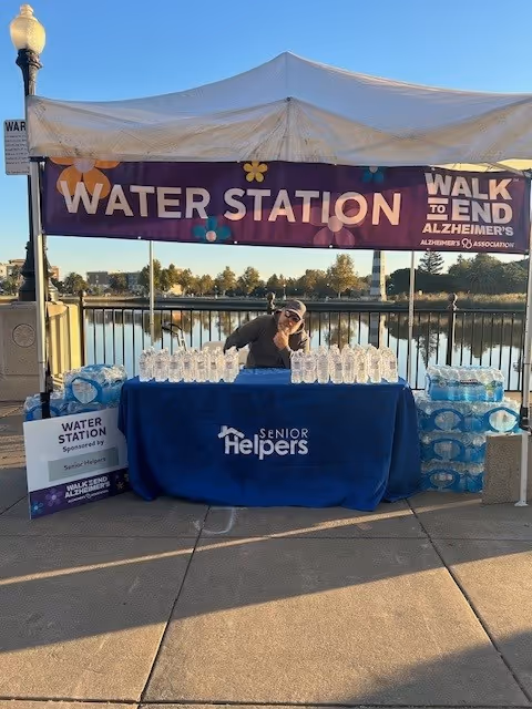 An outdoor water station setup under a tent with a Senior Helpers banner.