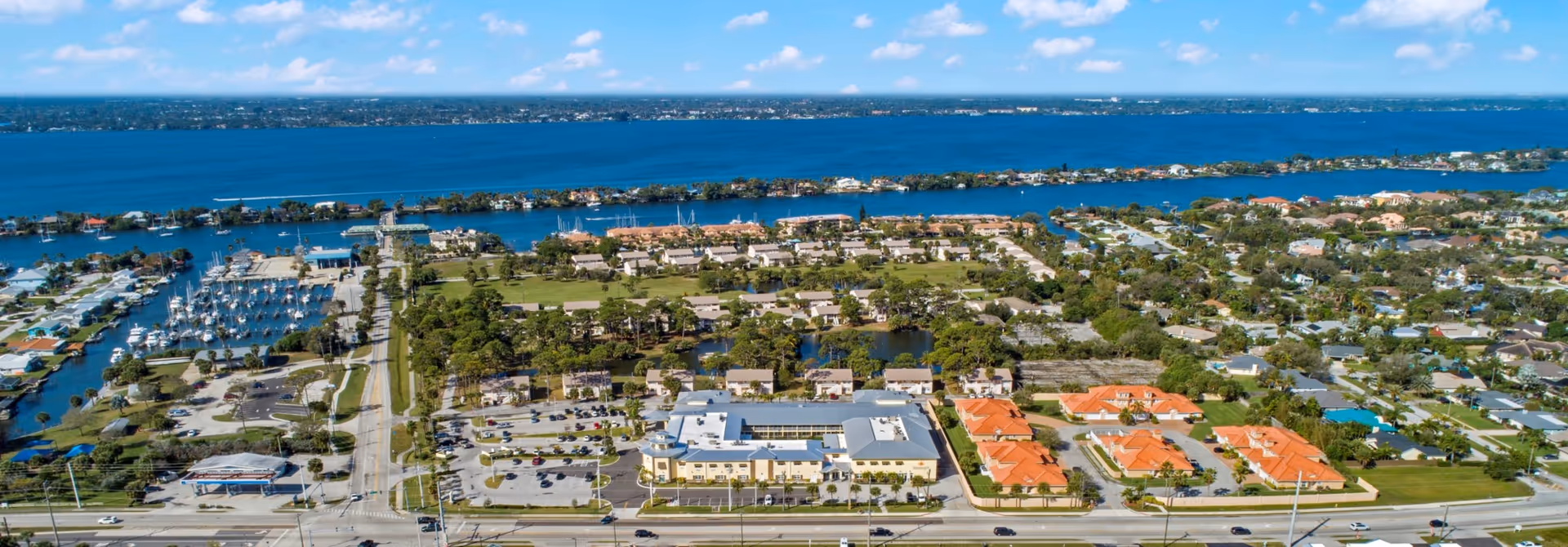 Aerial view of a coastal neighborhood with water, marina, and red-roofed buildings.