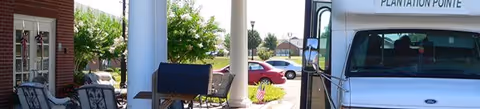 Outdoor entrance at The Arrington Assisted Living Community, with seating and a parked vehicle.