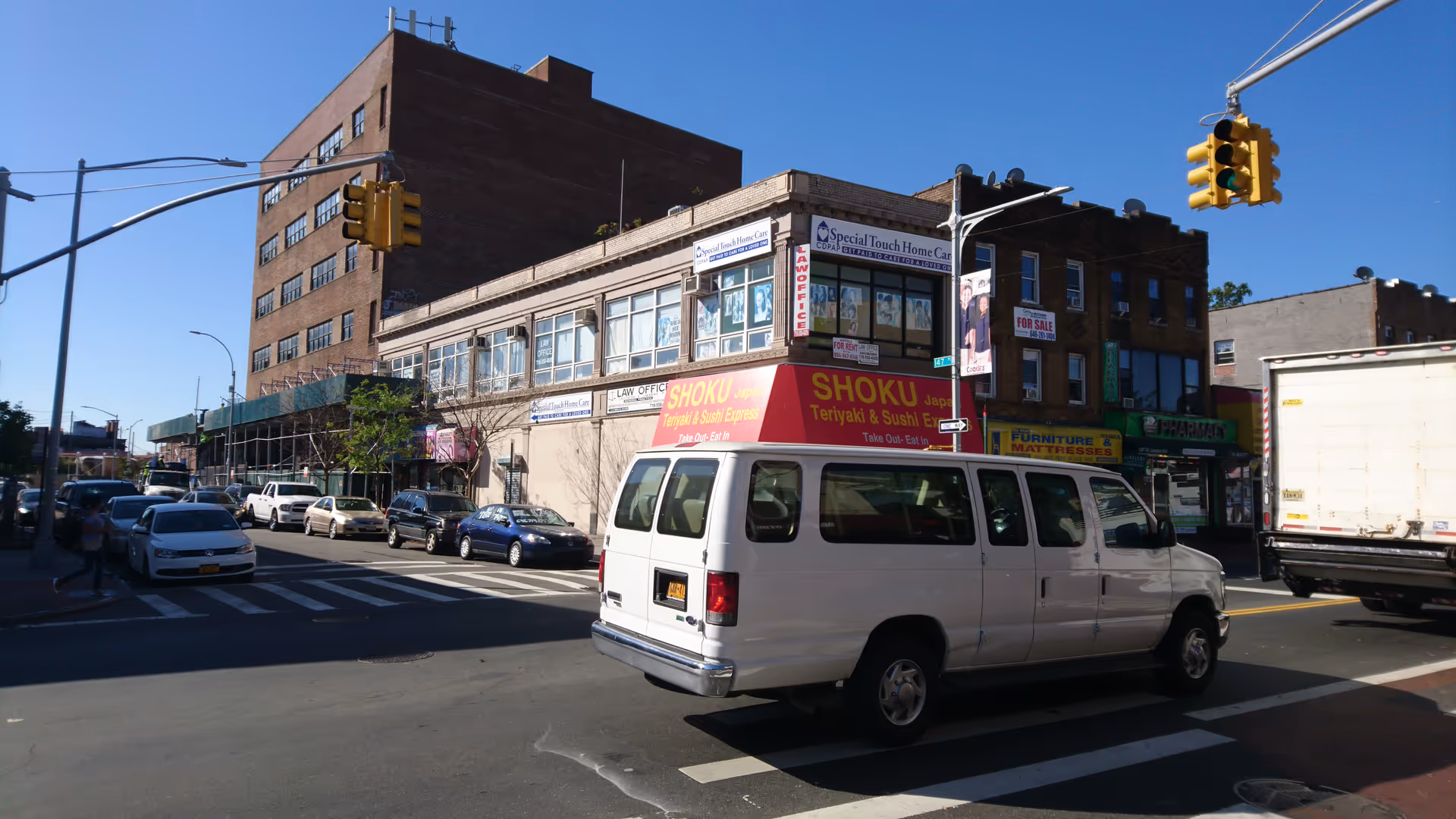 A white van drives by a brick storefront building on a busy city street.