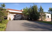 Exterior view of Autumn Lake Healthcare at Norwalk entrance with driveway, trees, and clear sky.