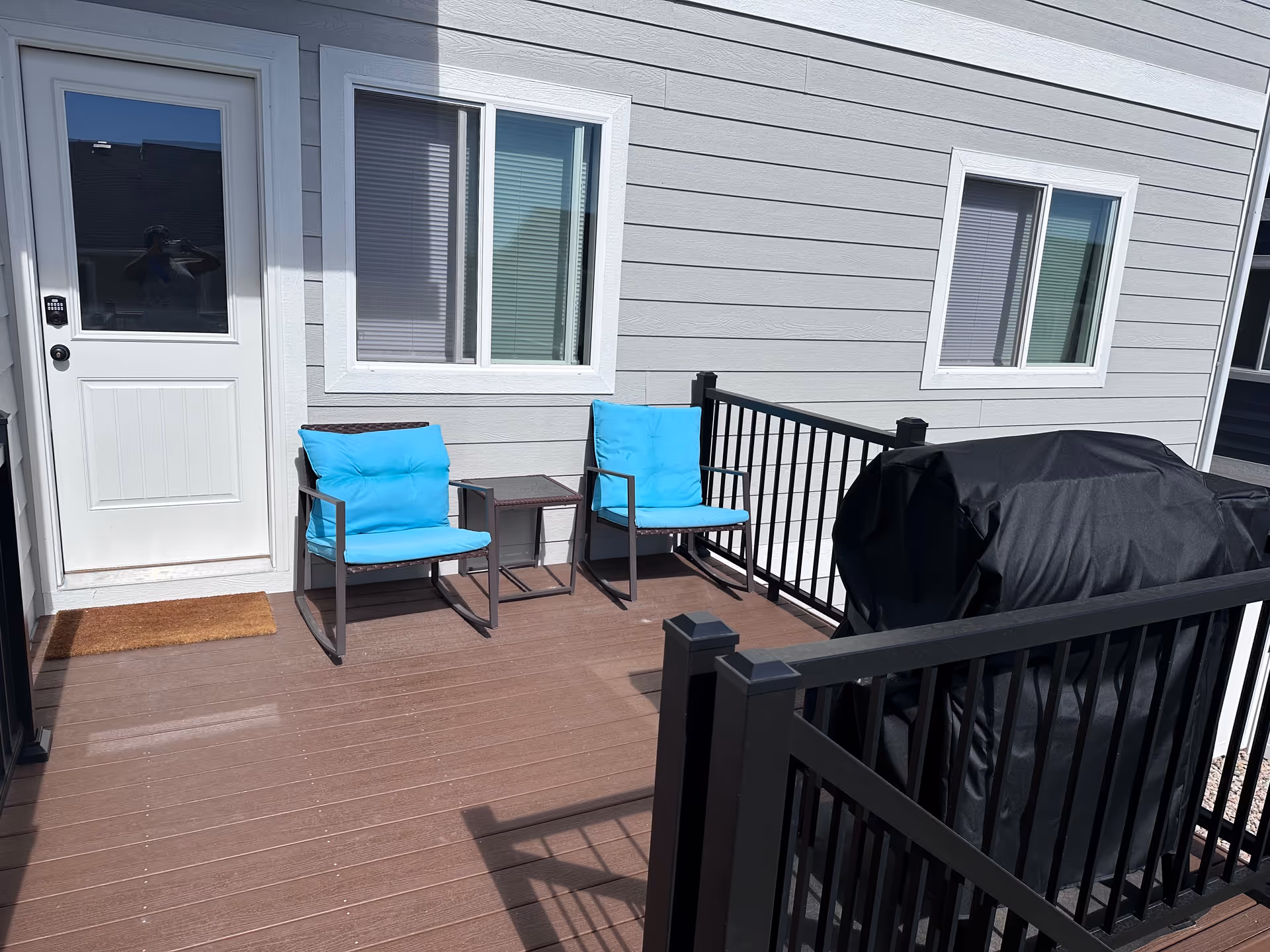 Outdoor deck with two blue cushioned chairs, a small table, and a covered grill.