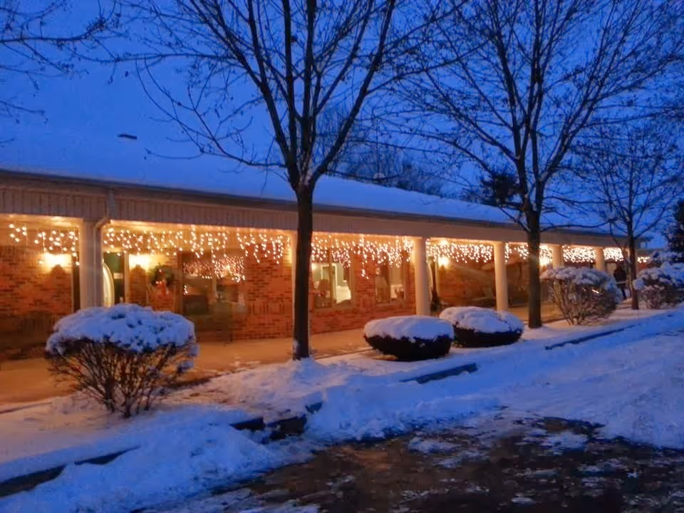 Snow covers the brick building's front walkway, with twinkling string lights.