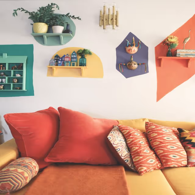 Colorful living room sofa with red and patterned pillows beneath decorative wall shelves and small ornaments.