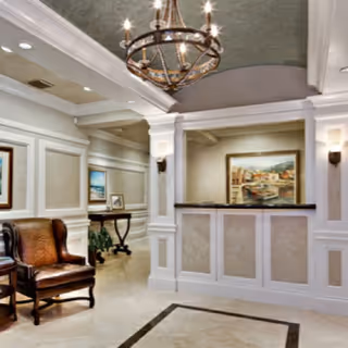Elegant senior living lobby with chandelier, reception desk, and leather chairs.
