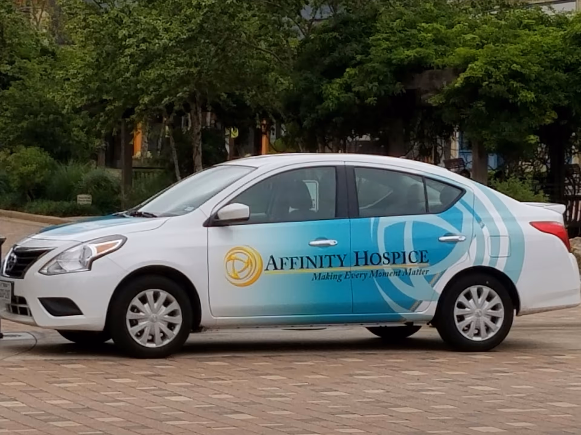 White Affinity Hospice car with teal waves parked outdoors near trees