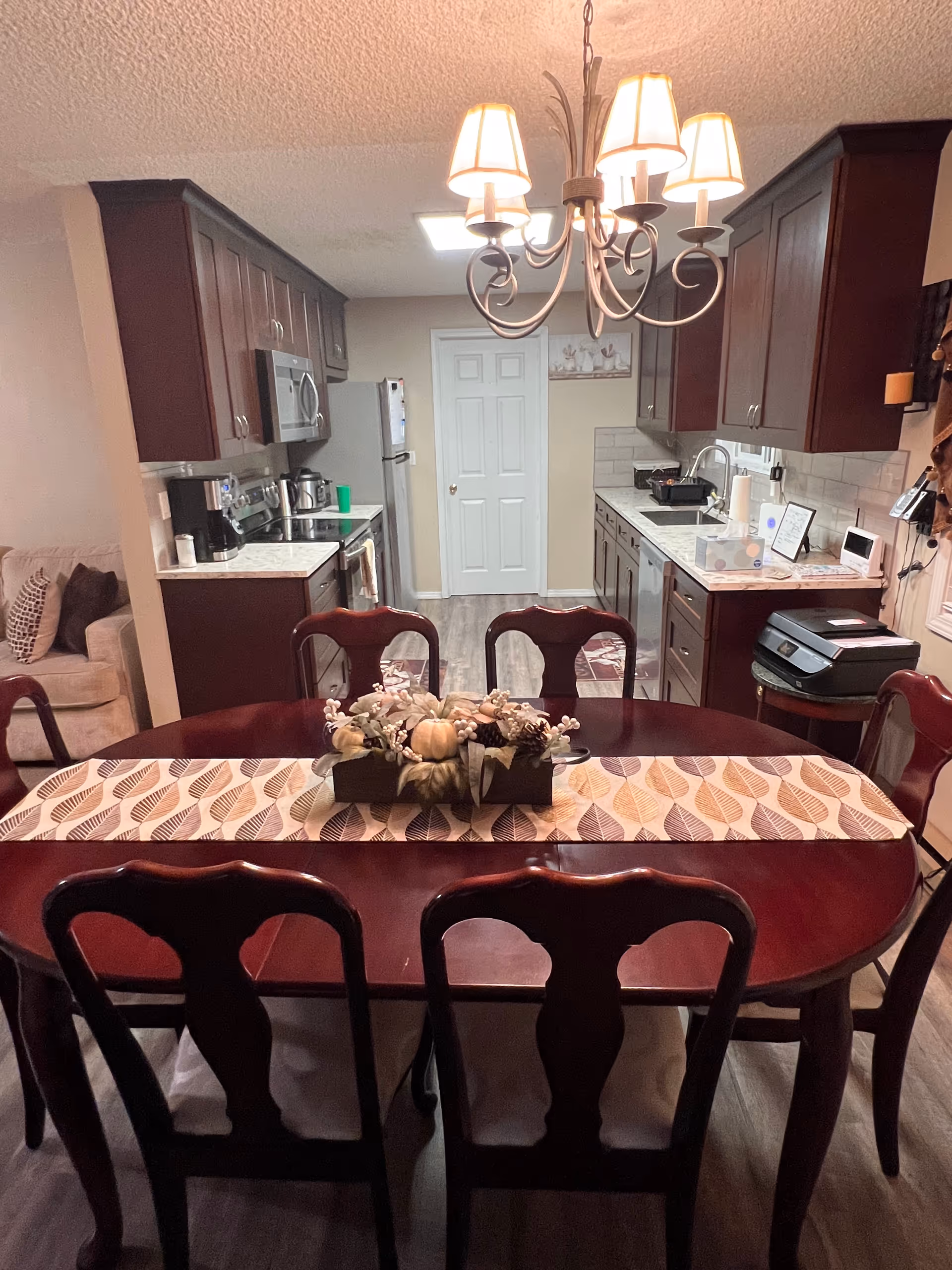 A dark wooden dining table with chairs in a kitchen and dining area under a chandelier.