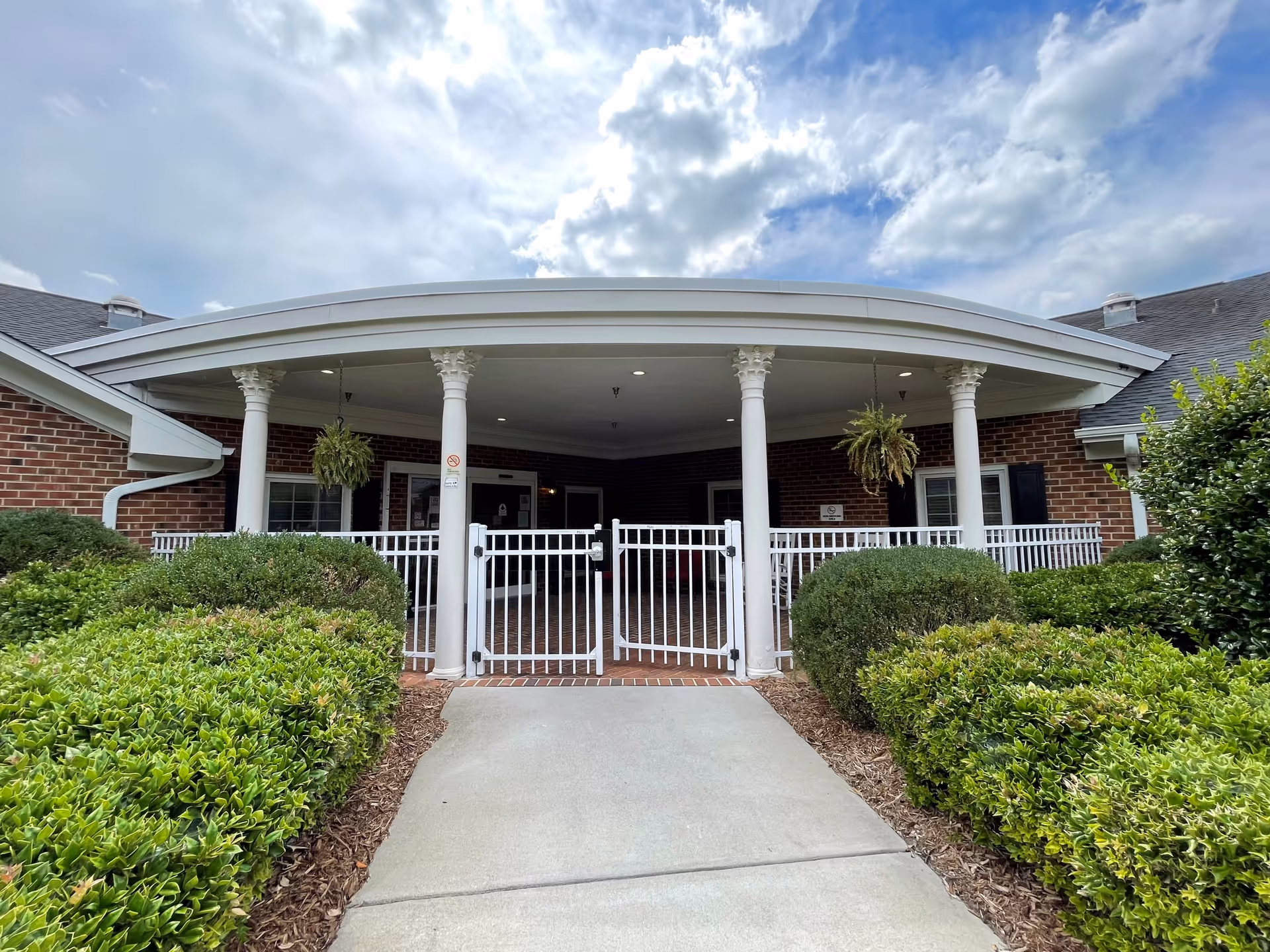 Brick senior care facility with a covered, columned entrance and white gate.