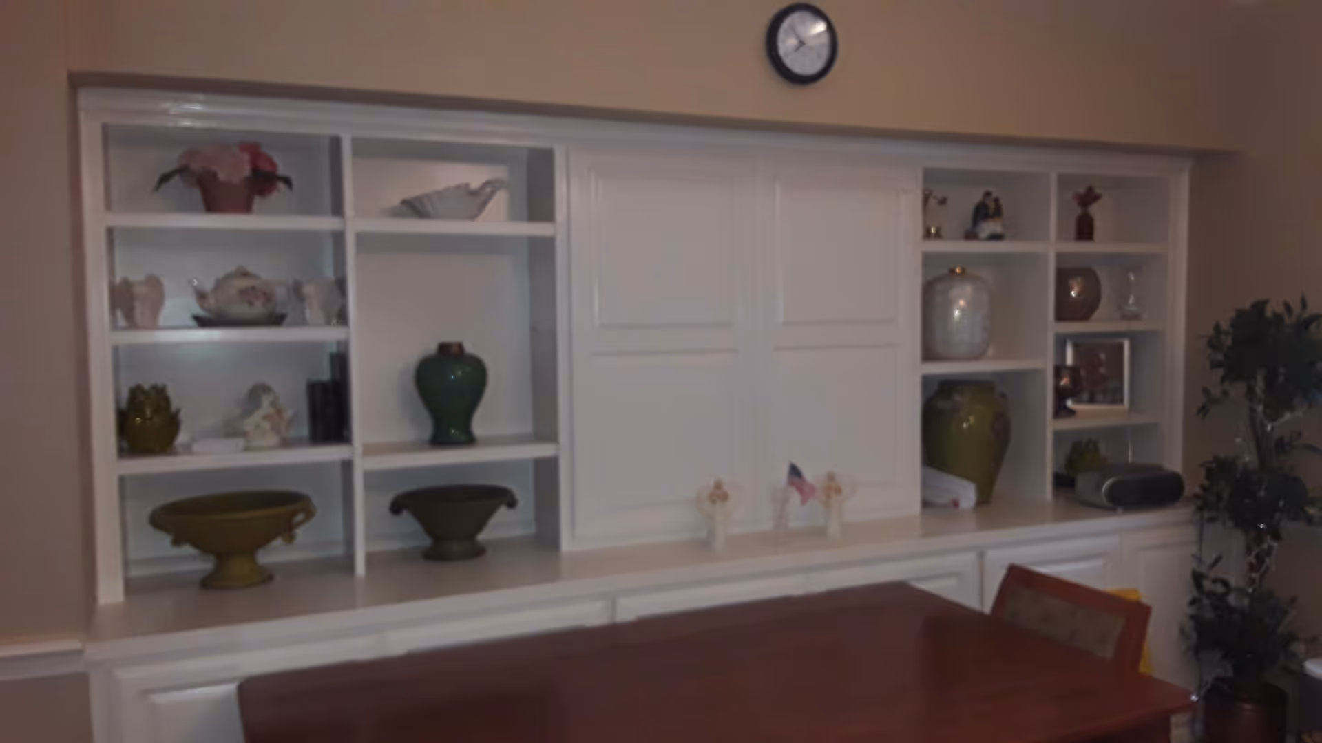 A white built-in cabinet with decorative items sits above a wooden dining table.