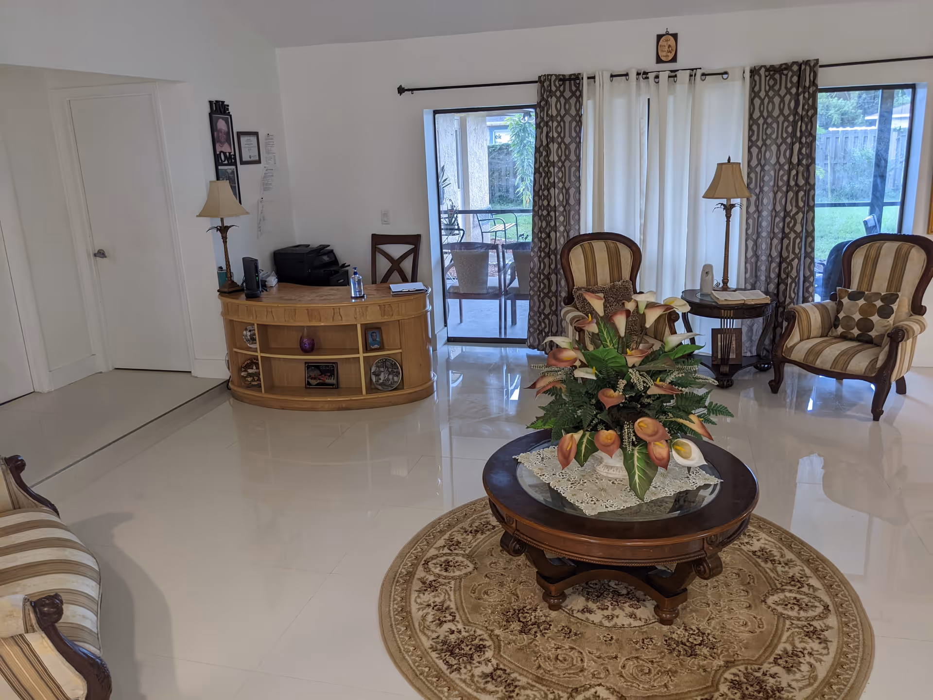 Bright living room lobby with circular floral centerpiece, two striped chairs, and sliding glass doors.