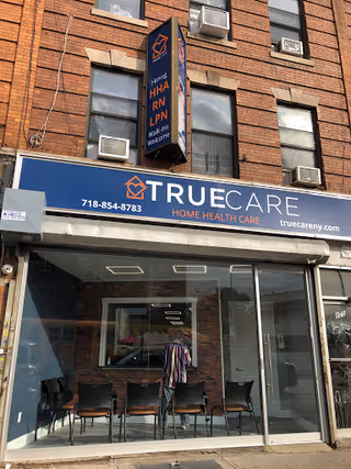 Brick storefront with blue TrueCare sign, glass entrance, and chairs visible inside.