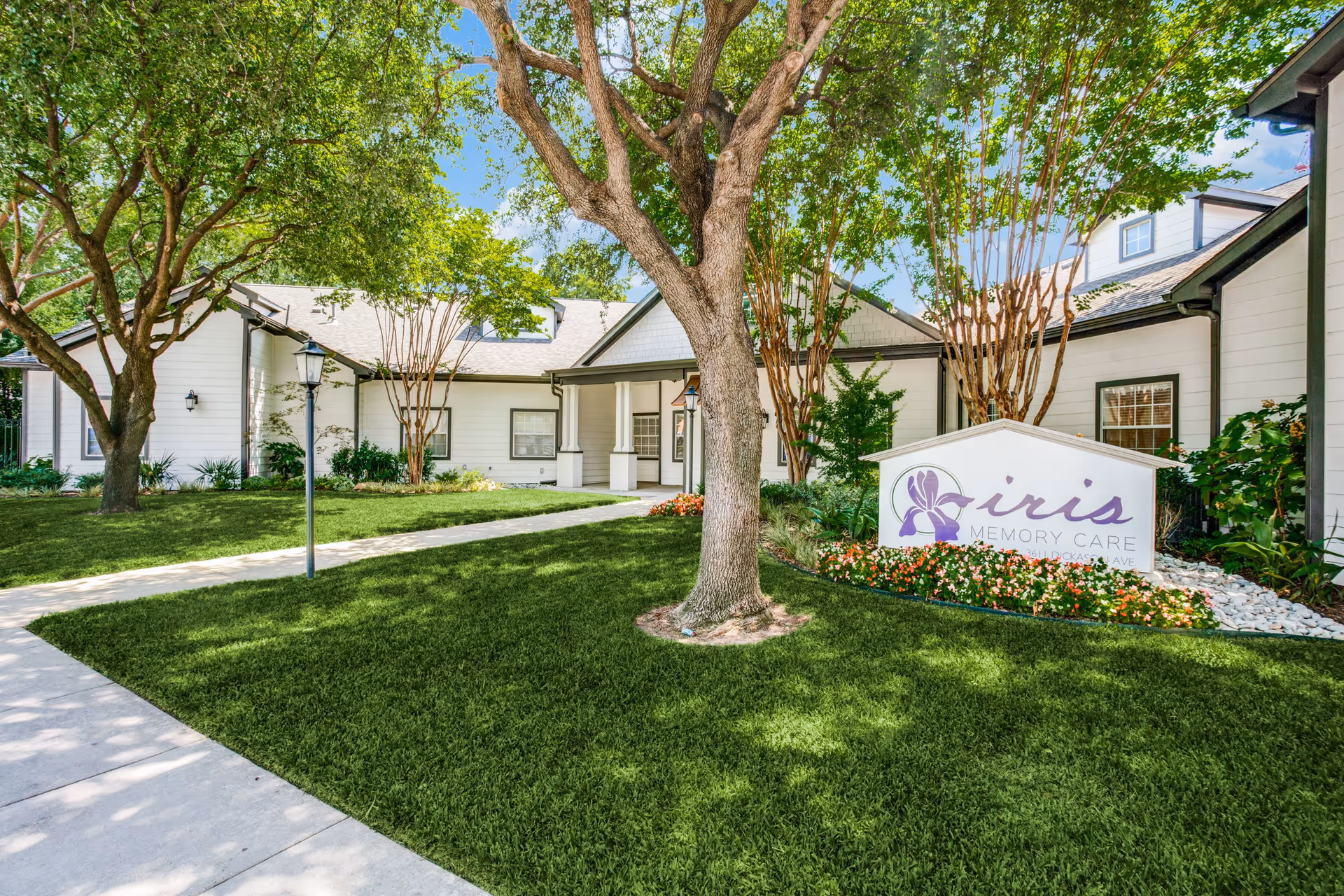 Exterior front of a memory care community showing a landscaped lawn, trees, a walkway, and a sign reading 'iris Memory Care'.