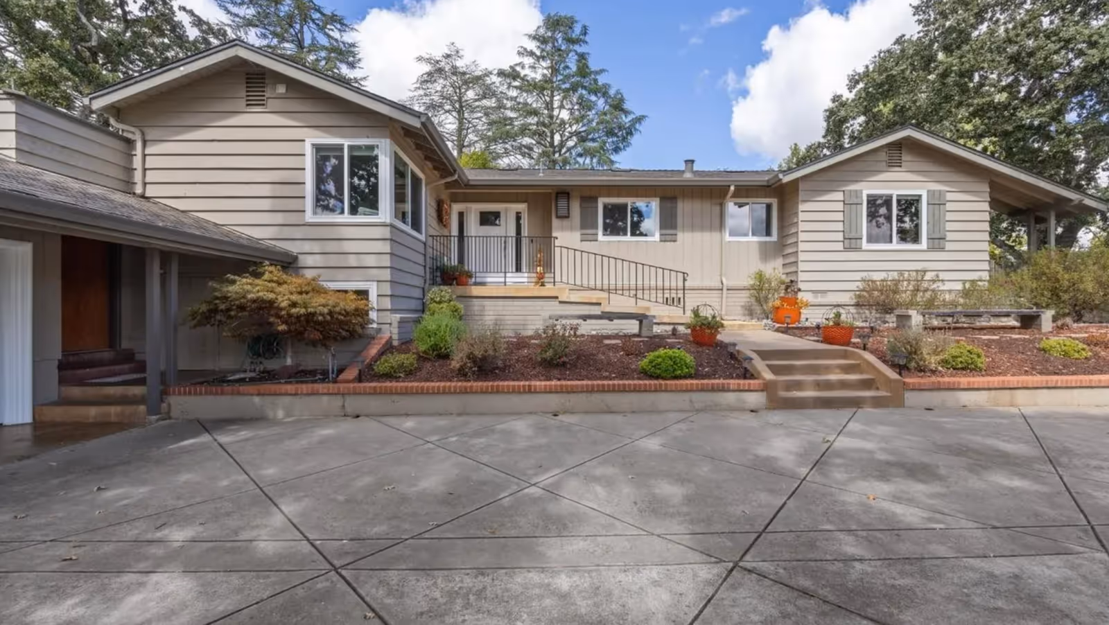 Single-story beige senior living facility exterior with steps, garden beds, and a wide driveway.