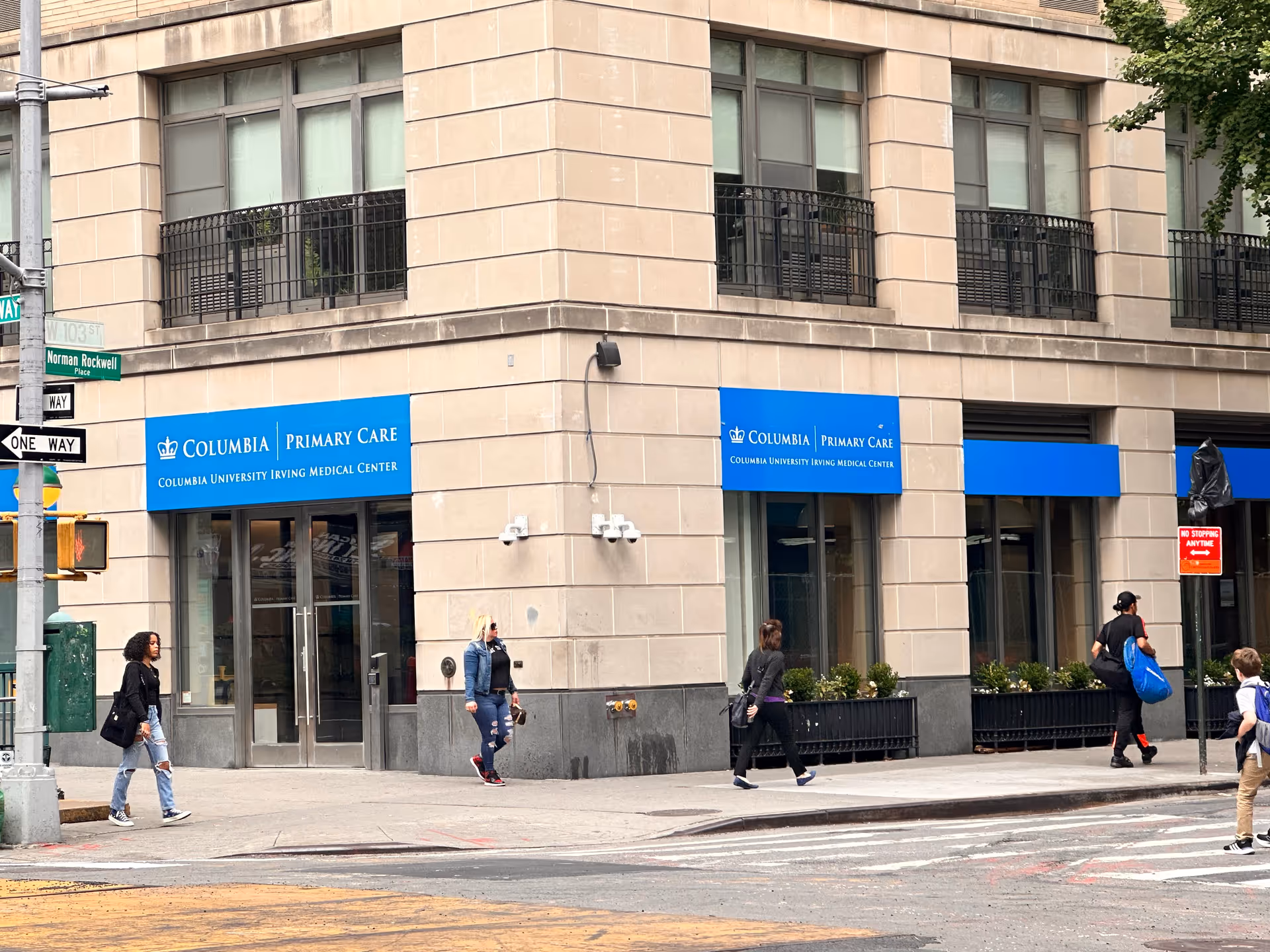 Exterior view of a beige building with blue Columbia Primary Care signs and pedestrians.