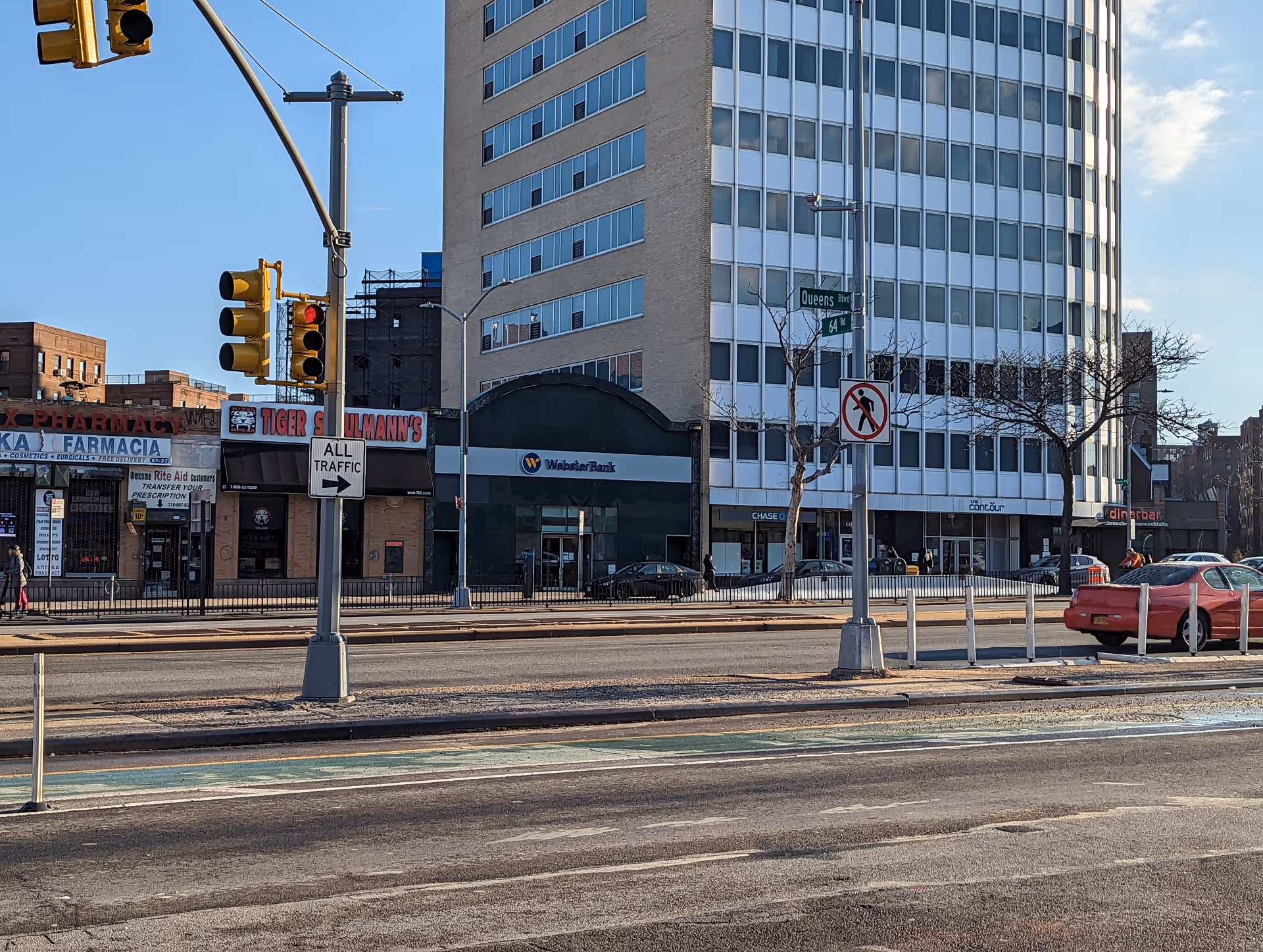 Urban street scene with a tall glass-fronted building and storefronts along the sidewalk.