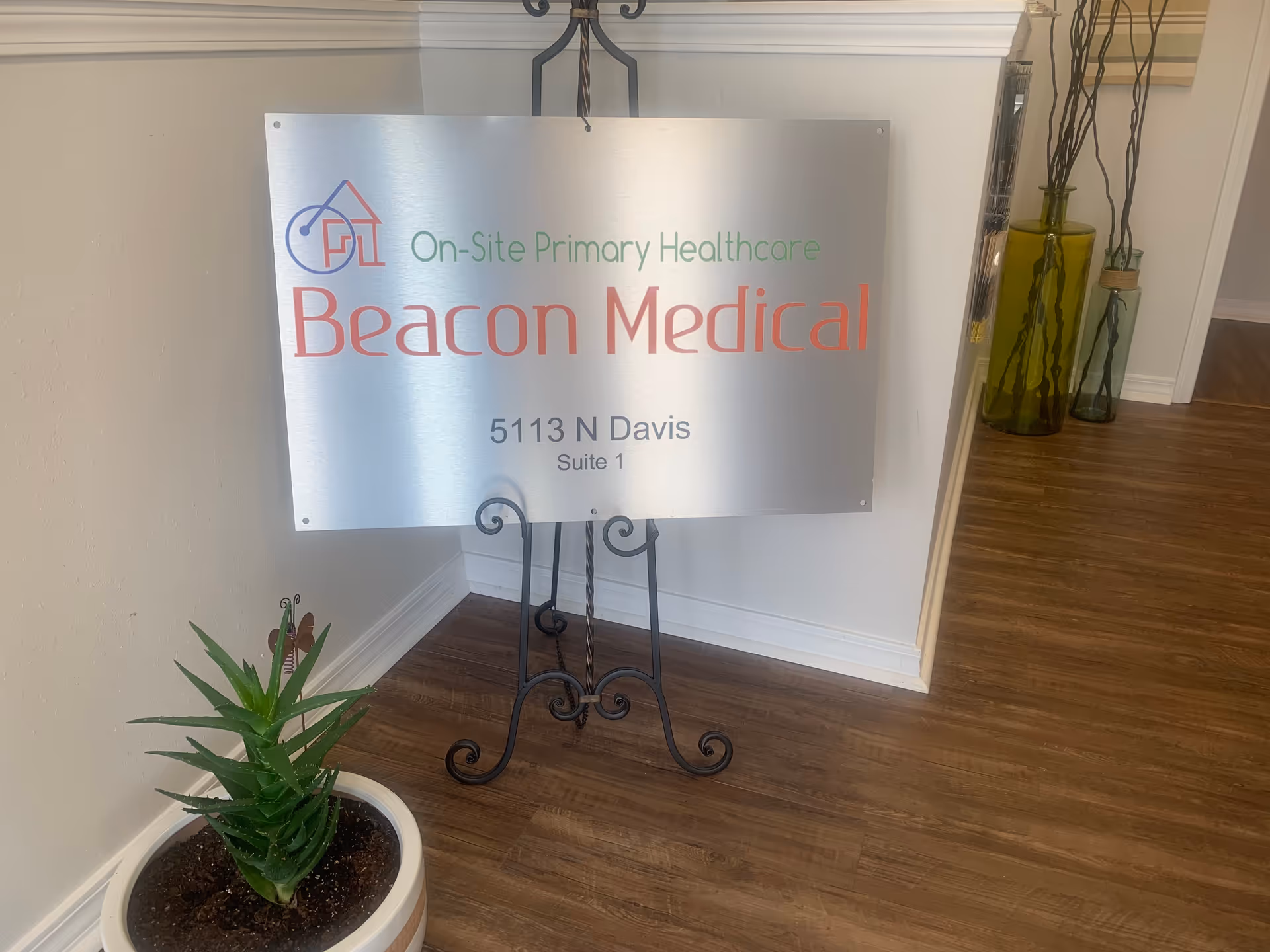 Metal Beacon Medical sign on a stand in a hallway beside a potted plant.