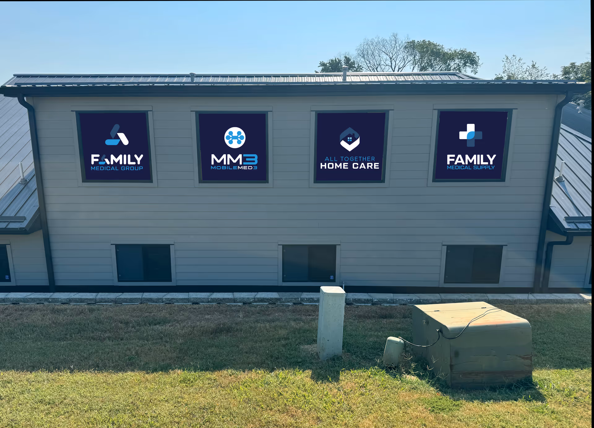 Exterior view of a beige facility with four logo signs on the facade and blue sky.