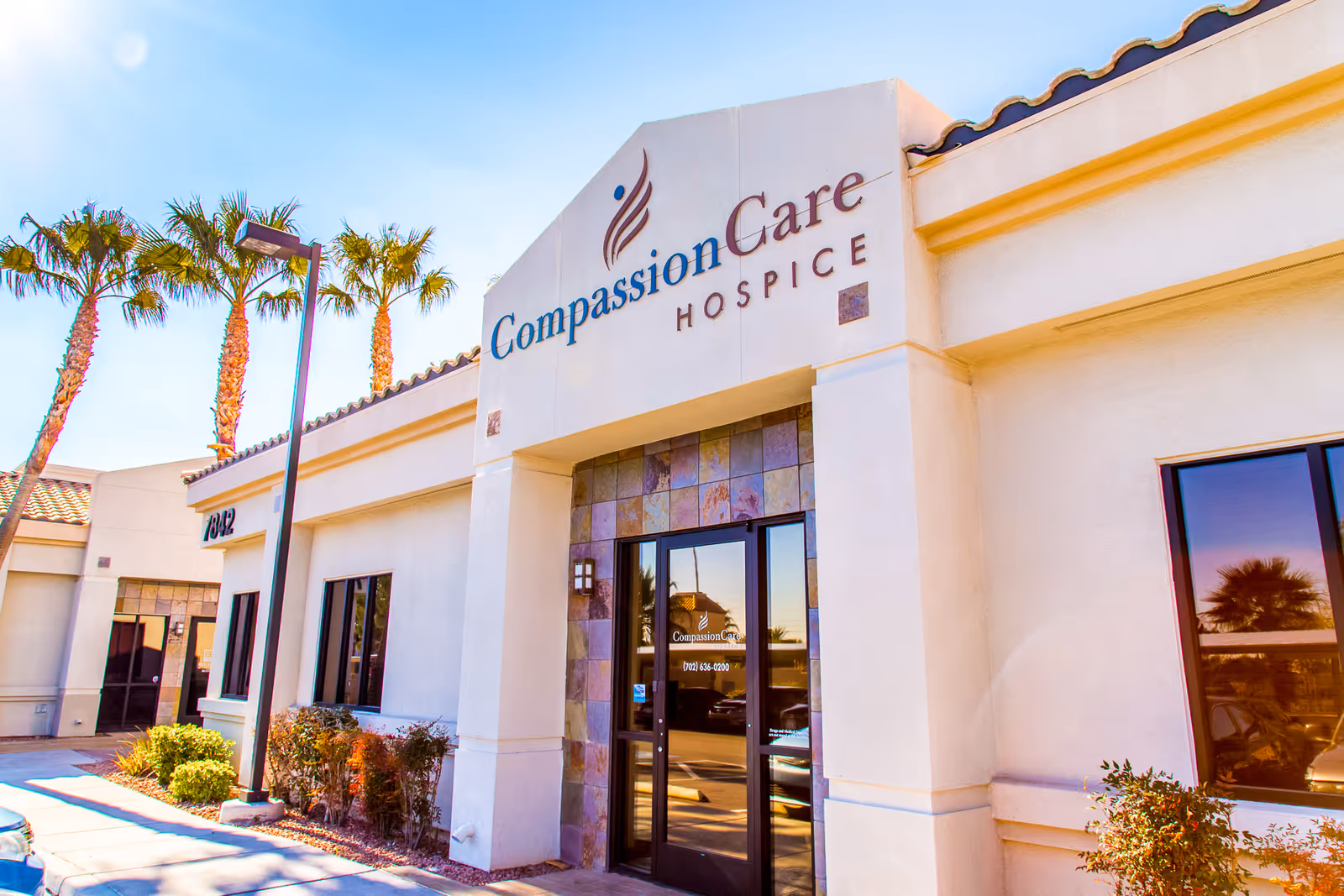 Exterior view of CompassionCare Hospice building with palm trees and a glass entrance.