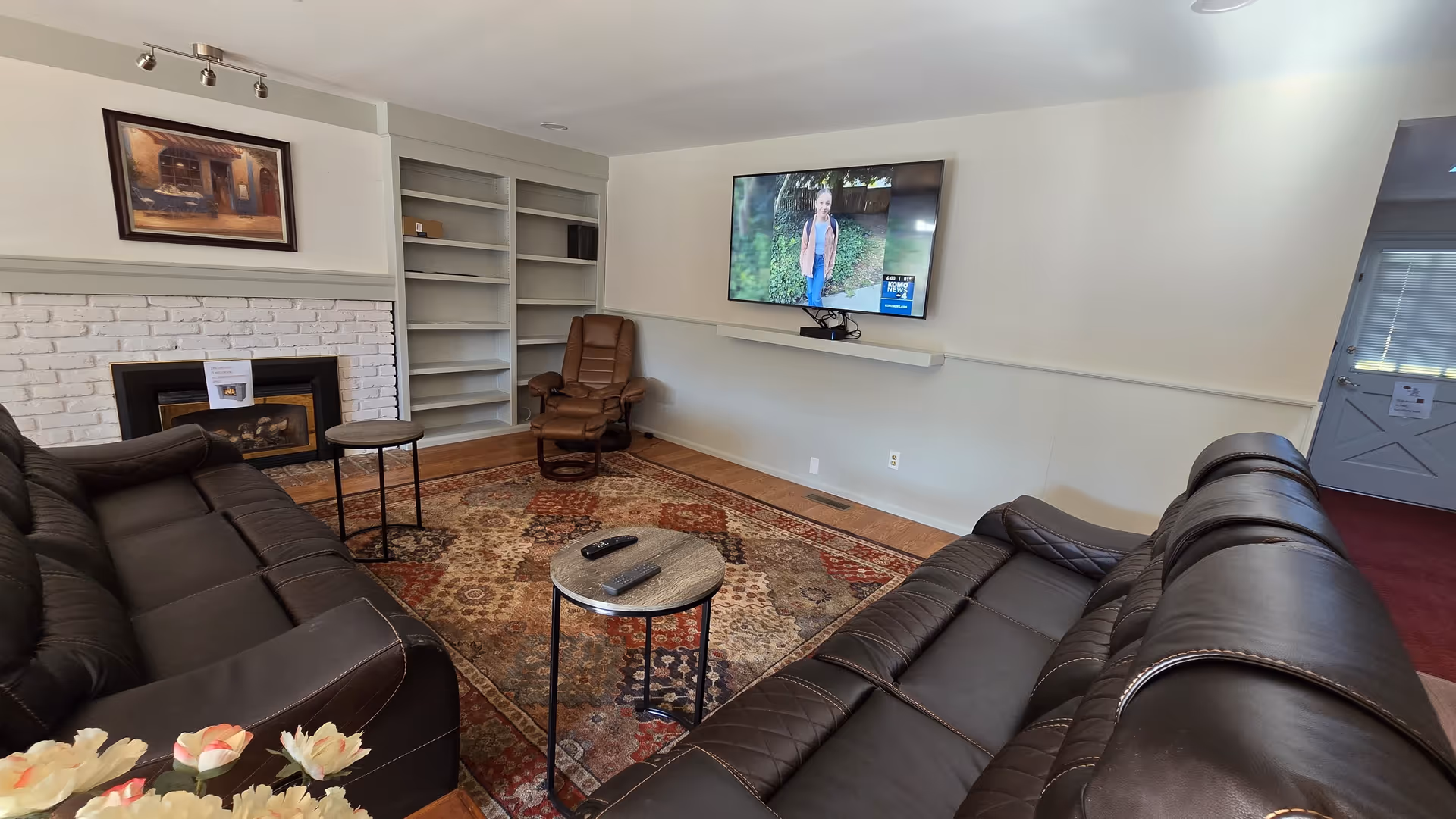 Cozy living room with leather sectional, fireplace, shelves, and wall-mounted TV.