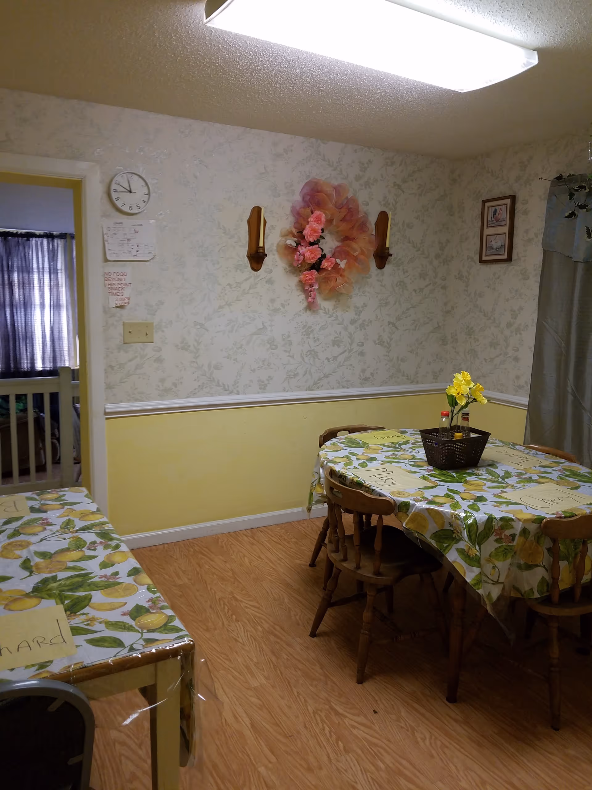 A small dining room in a senior care home with floral wallpaper.