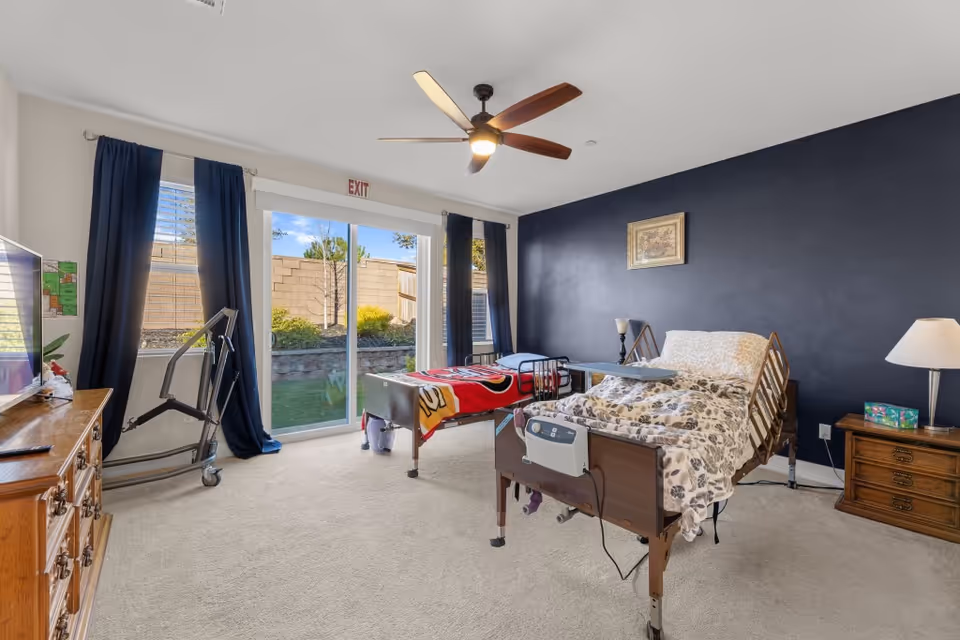 A single bedroom with a hospital-style bed, dark blue wall, curtains, and a sliding glass door.