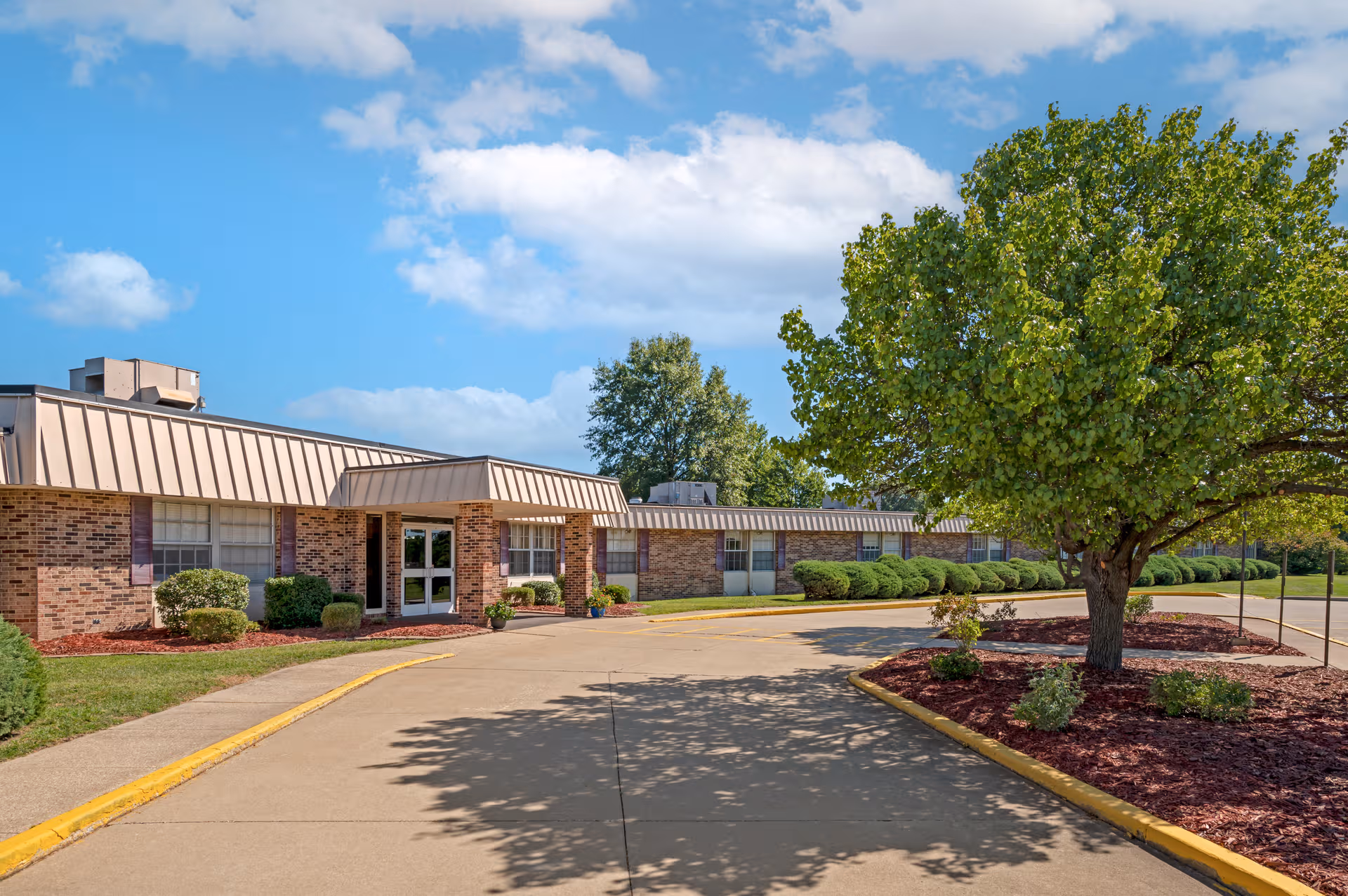 Single-story brick building with a covered entrance, parking lot, and surrounding trees.