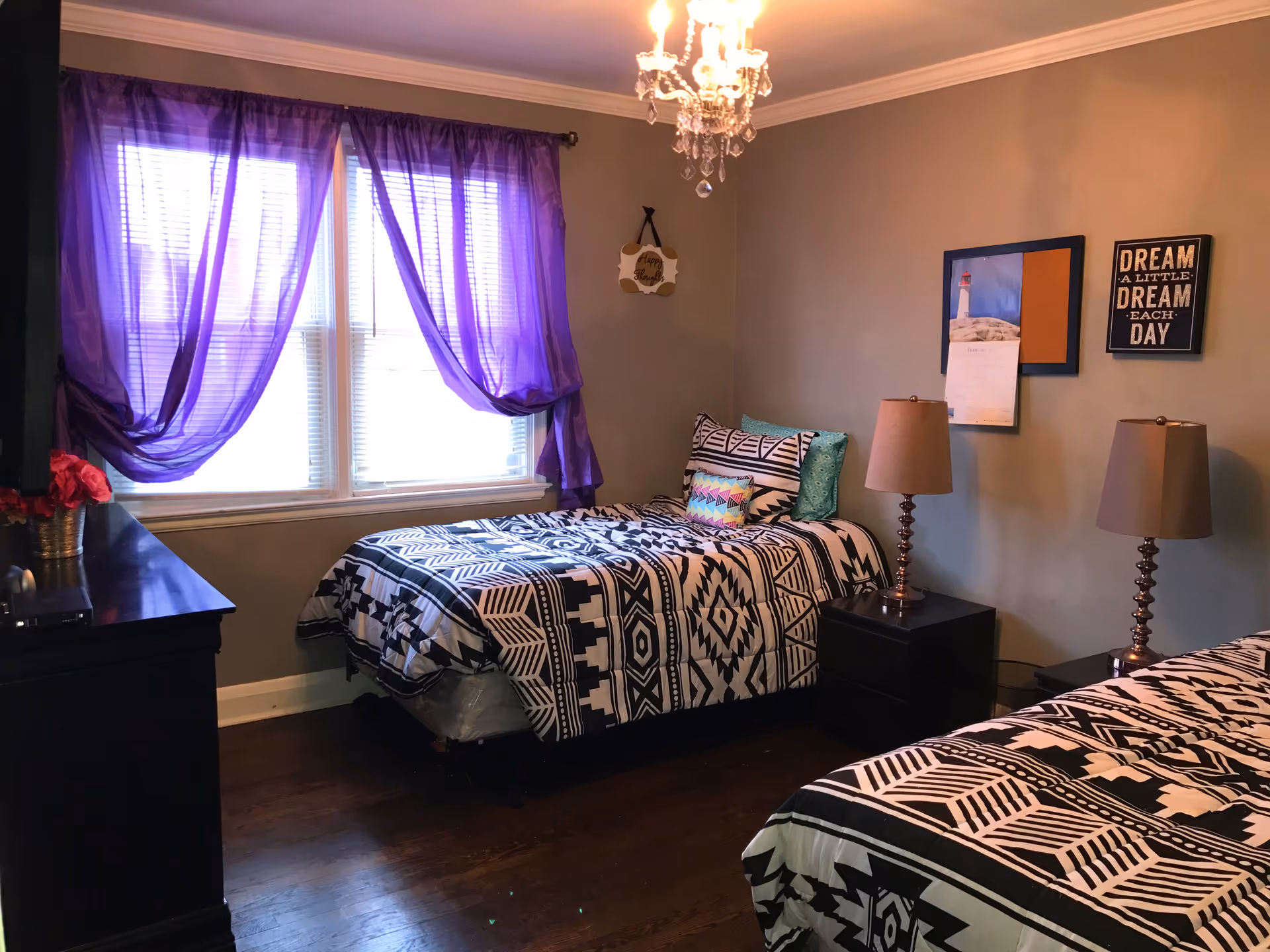 Twin beds with geometric bedding in a bedroom featuring purple curtains and lamps.